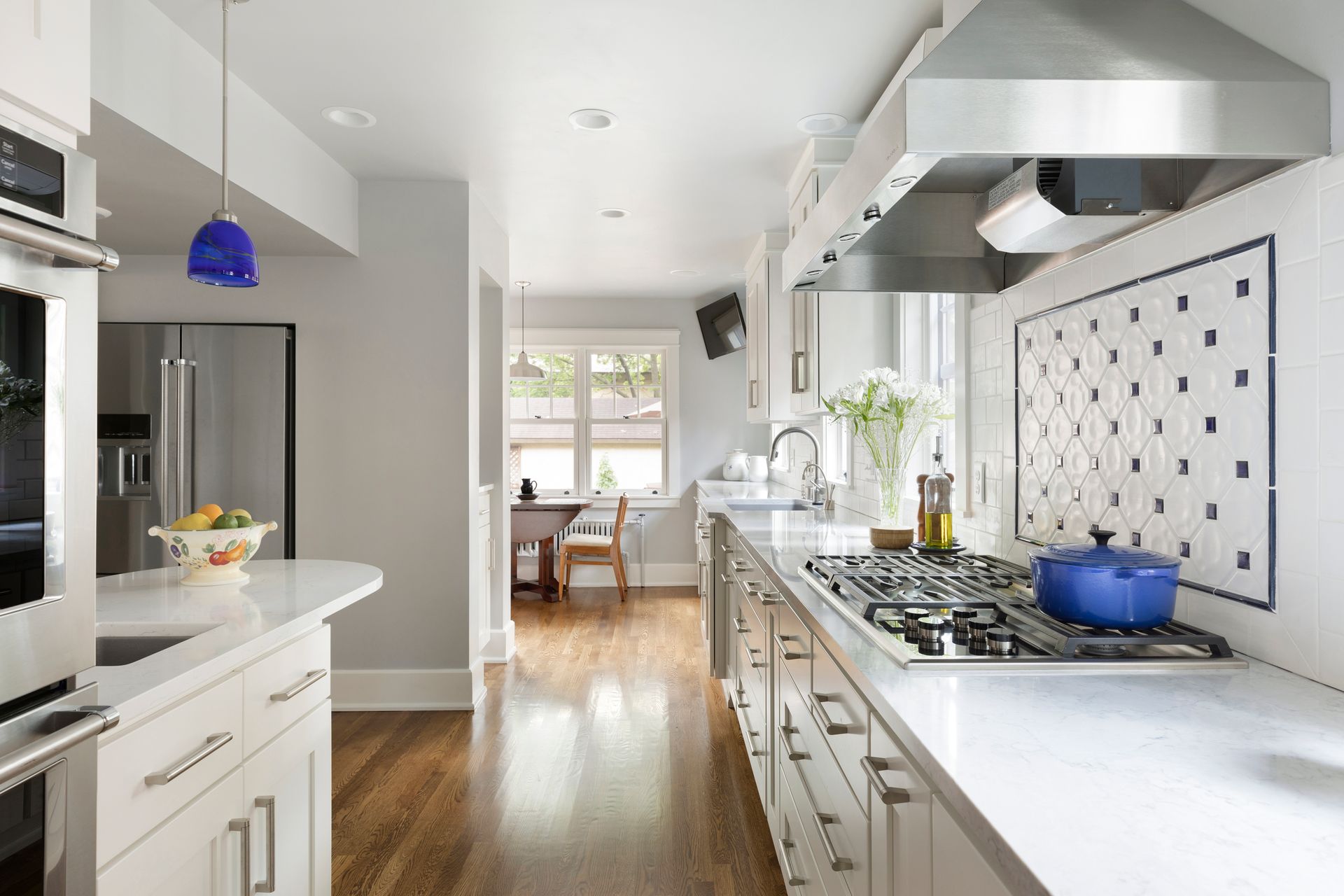 Bright, narrow kitchen with white cabinets, stainless steel appliances, and a blue pendant light.