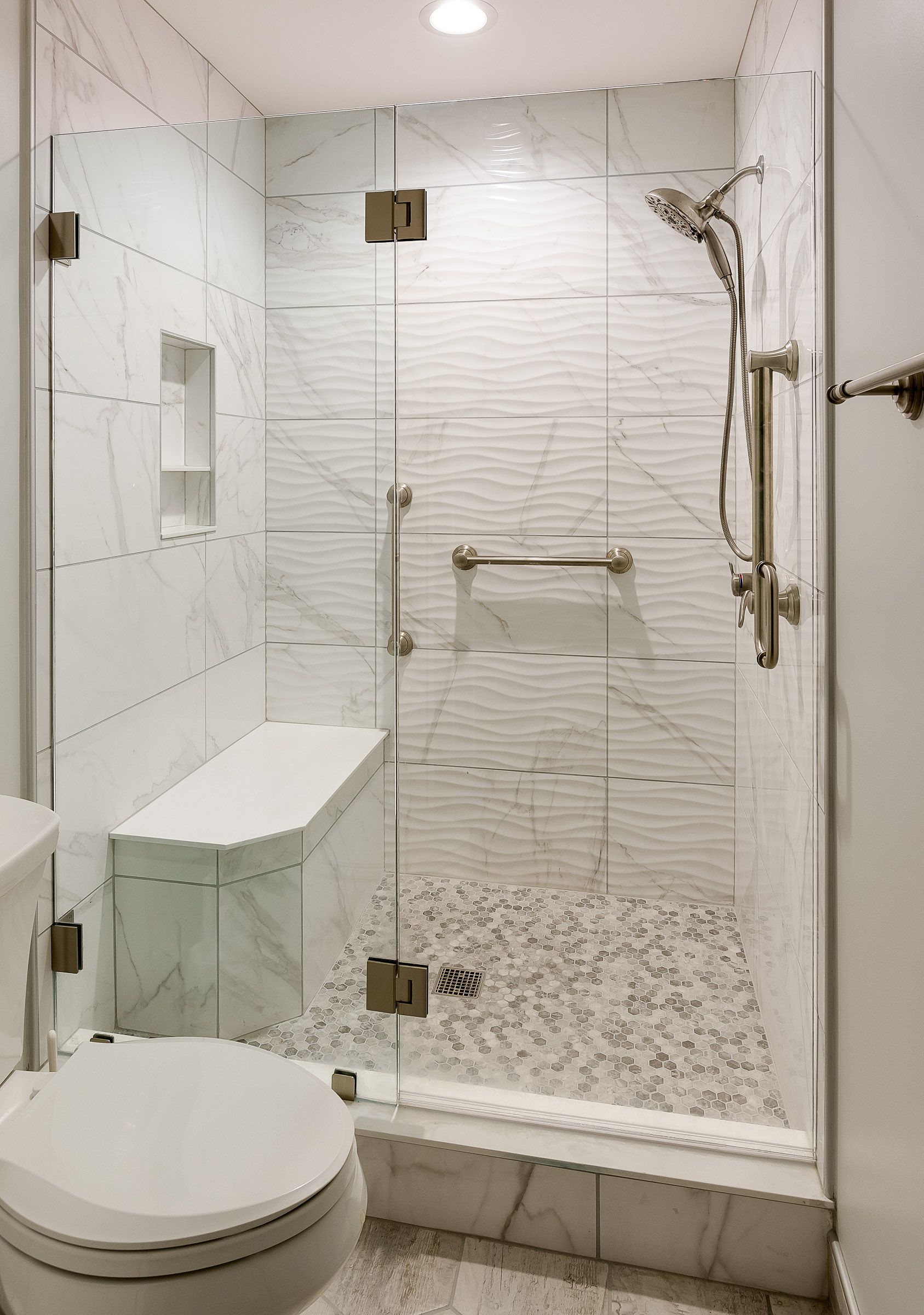 Modern accessible shower with glass doors, built-in bench, grab bars, and textured white tile.