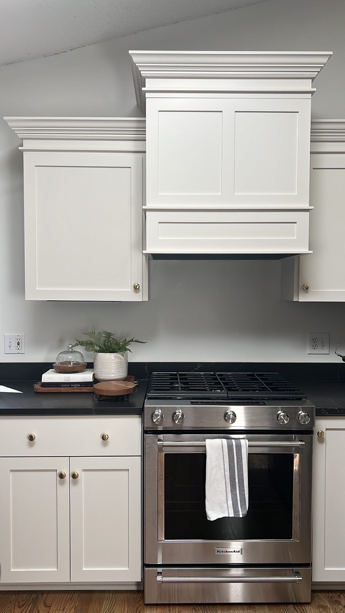 White kitchen cabinets with black countertop, stainless steel oven, and range hood.