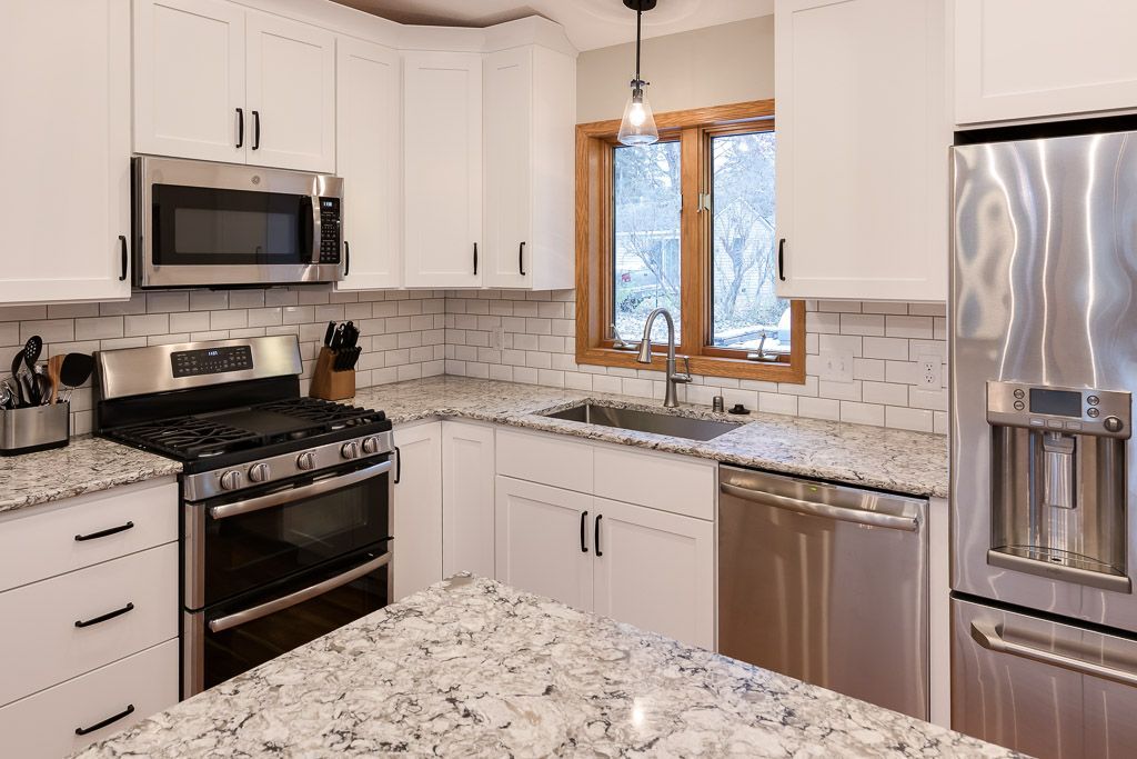 White kitchen with stainless steel appliances, granite countertops, and a window.