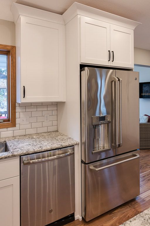 White kitchen cabinets above a stainless steel refrigerator and dishwasher with granite countertop.