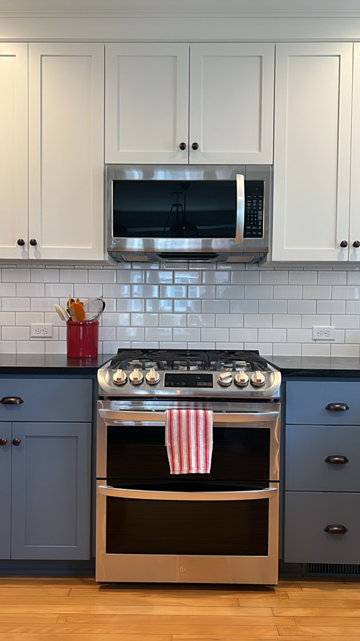 Kitchen with white upper cabinets, blue lower cabinets, stainless steel stove, and white subway tile backsplash.