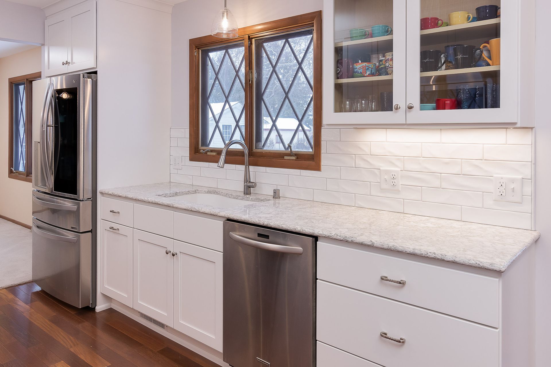 Modern kitchen with white cabinets, stainless steel appliances, and diamond-paned window above the sink.