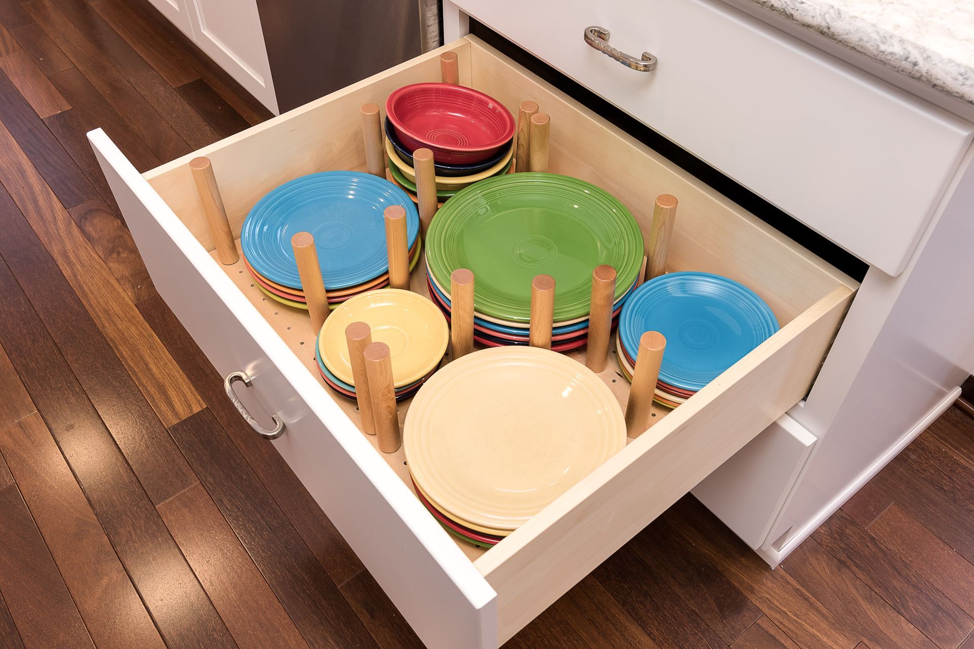 Drawer with plates separated by wooden pegs in a kitchen cabinet.