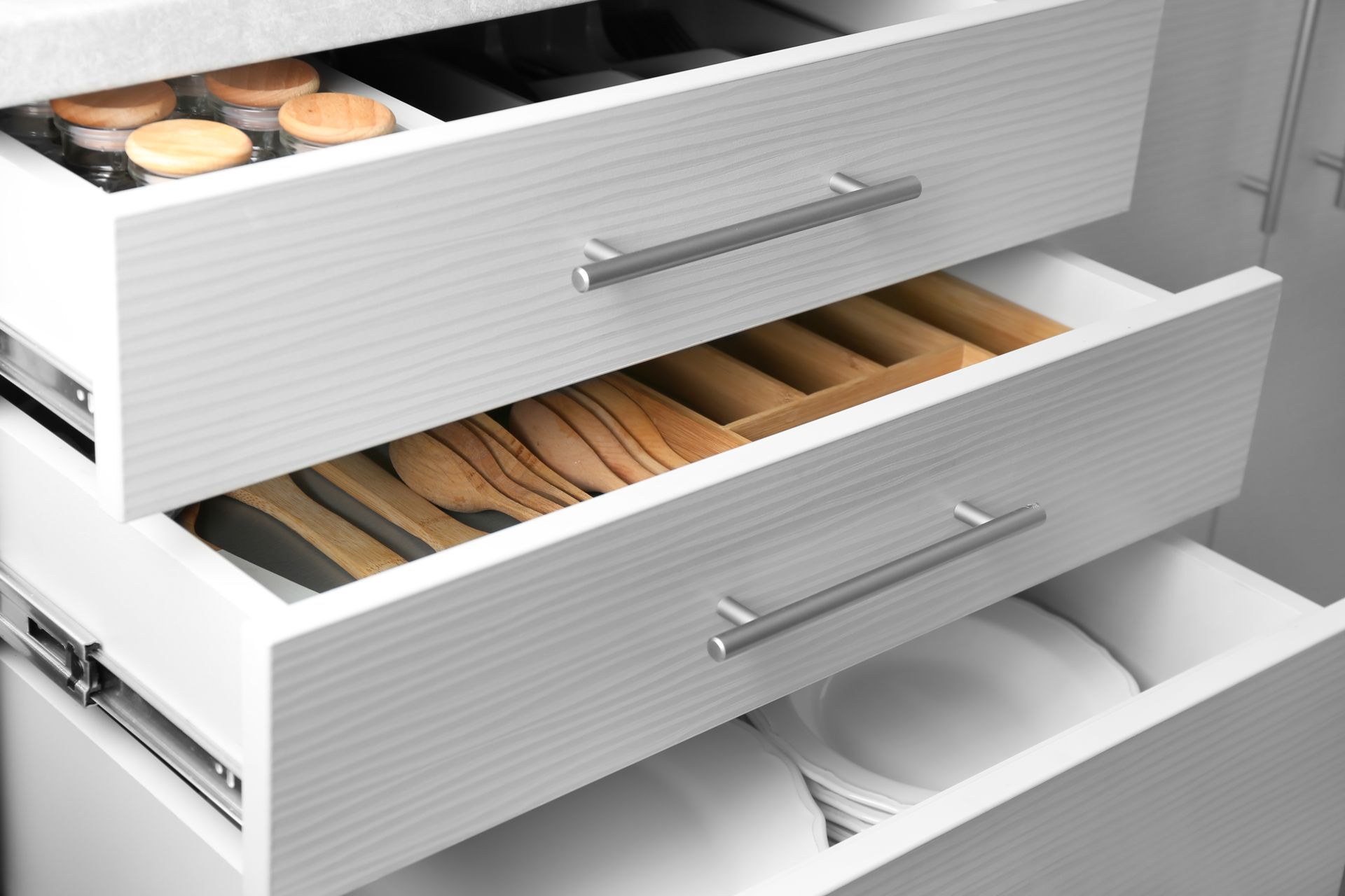 White kitchen drawers with utensils, plates, and jars.