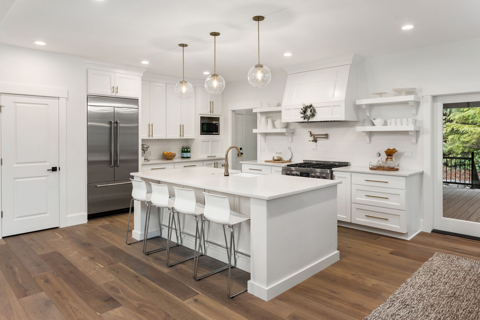 Modern white kitchen with island, wooden floors, stainless steel appliances, and pendant lights.