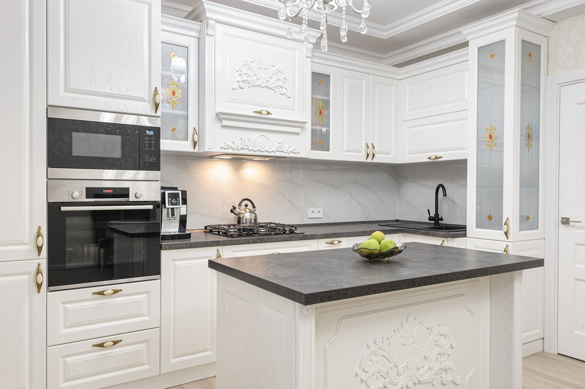 Elegant white kitchen with ornate cabinets, dark countertop, and an island.