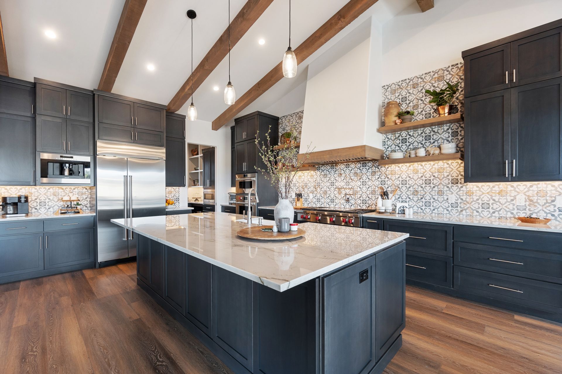 Modern kitchen with dark blue cabinets, large island, wood beams, and tiled backsplash.
