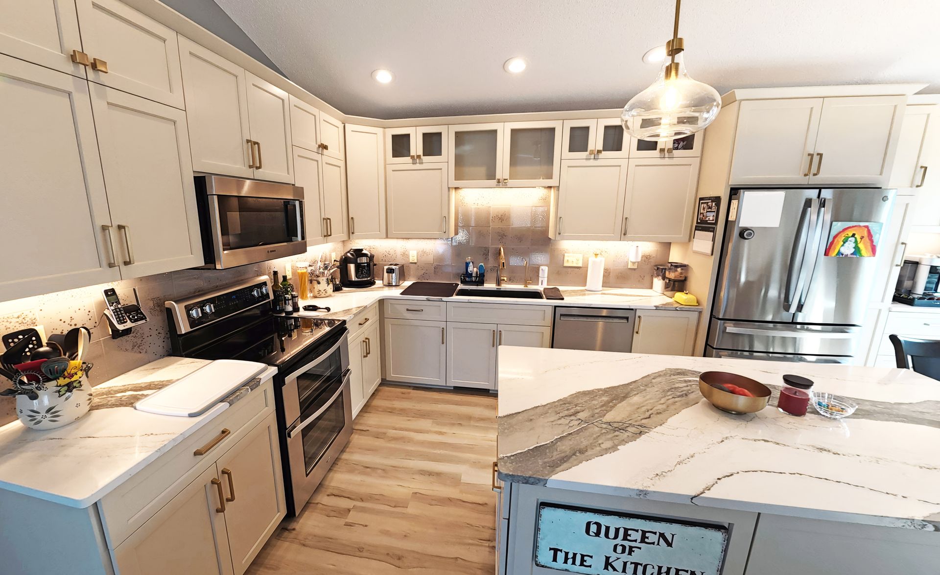White kitchen with stainless steel appliances, marble countertops, and light wood flooring.