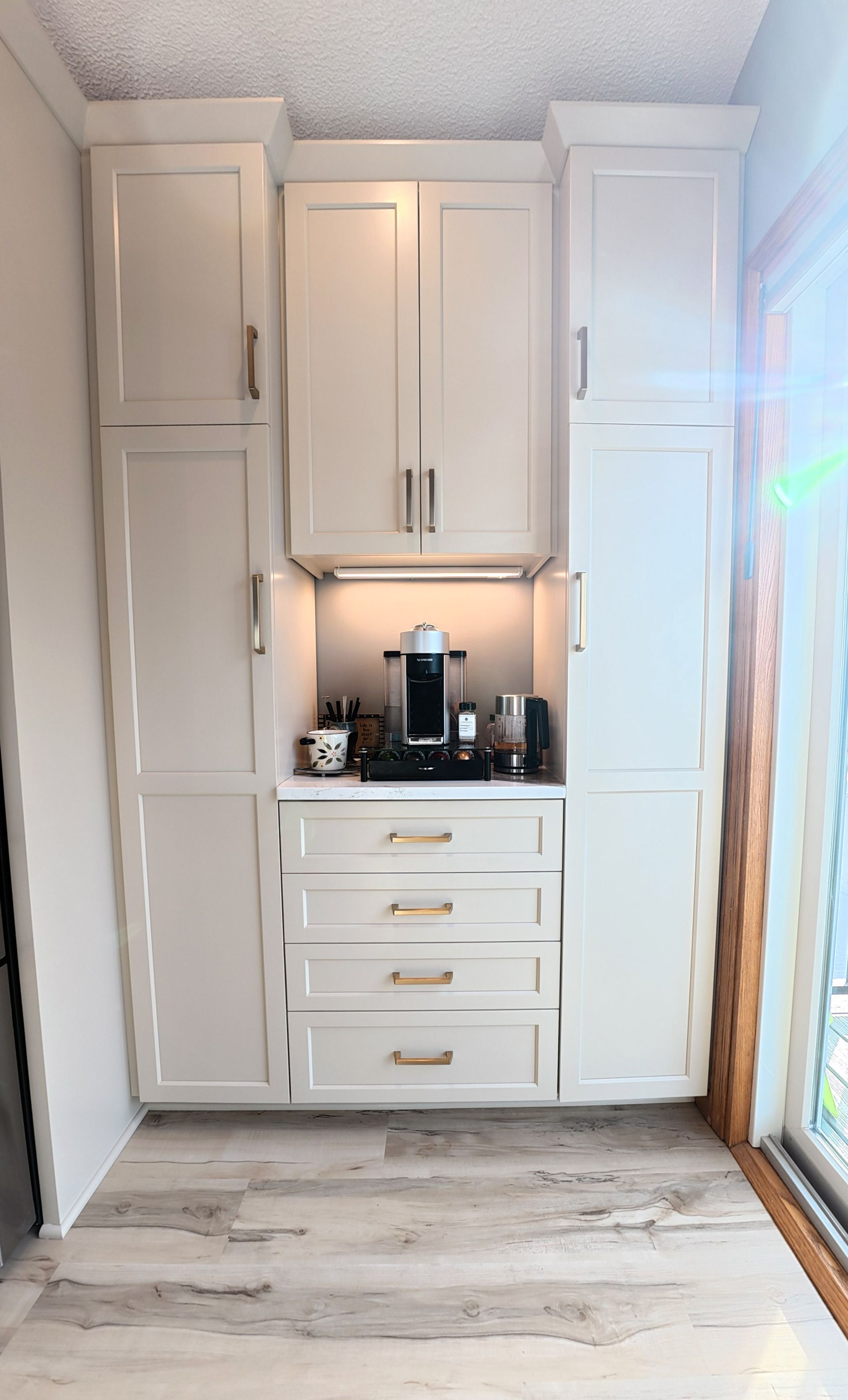 Cream-colored built-in kitchen cabinet unit with coffee station. Features drawers, upper cabinets, and a Keurig coffee maker.