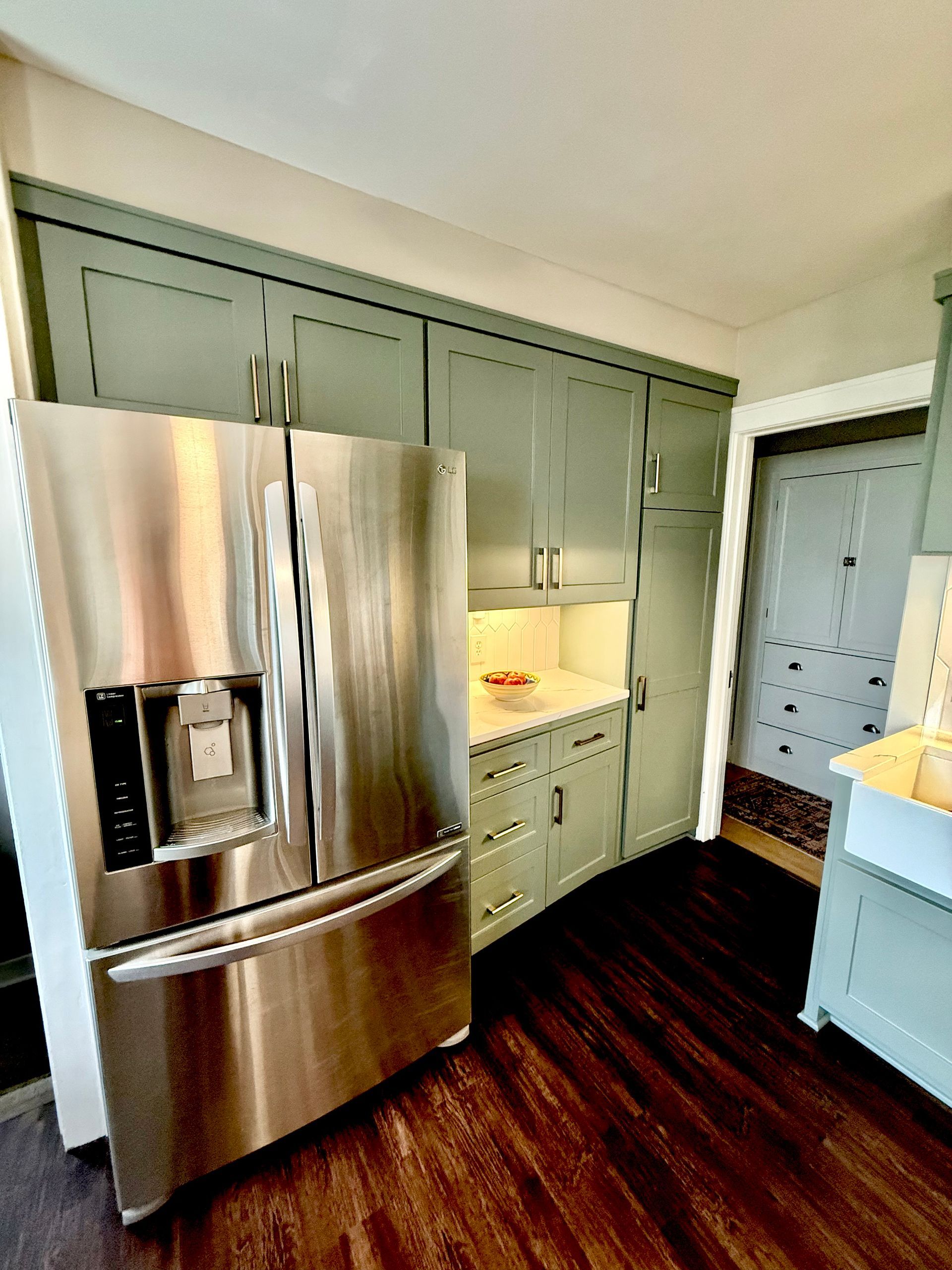 Kitchen with sage green cabinets, white backsplash, farmhouse sink, and wood flooring.