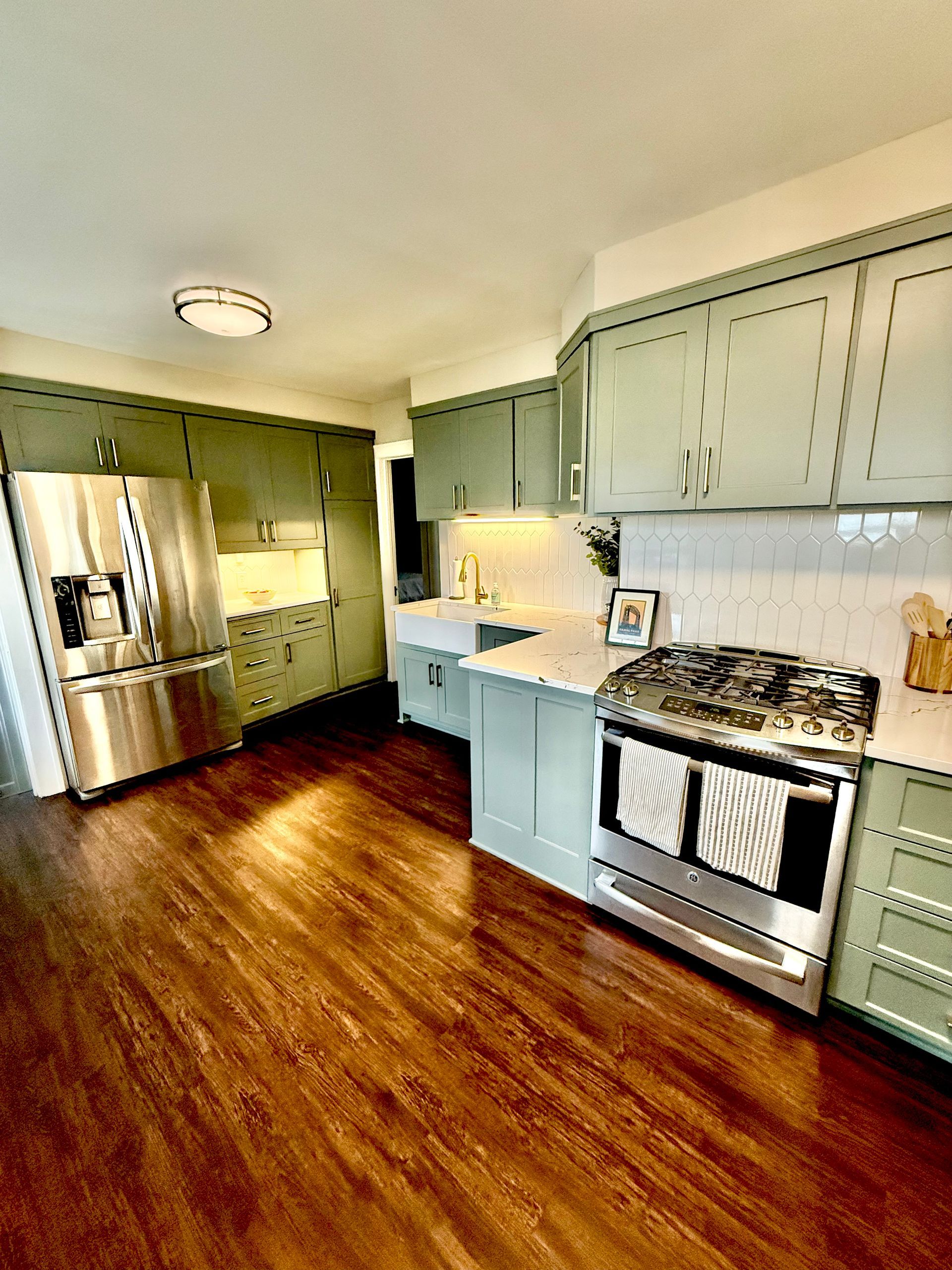 Kitchen with seafoam green cabinets, white backsplash, and wood-look flooring.