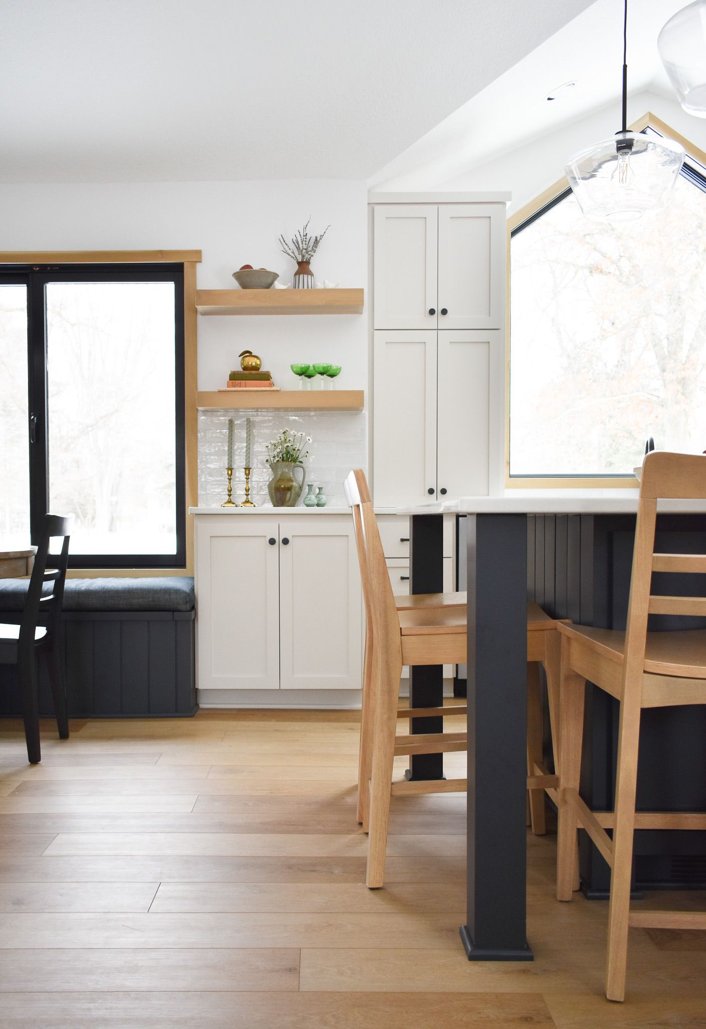Kitchen interior with wood floors, white cabinets, island with stools, and large windows.