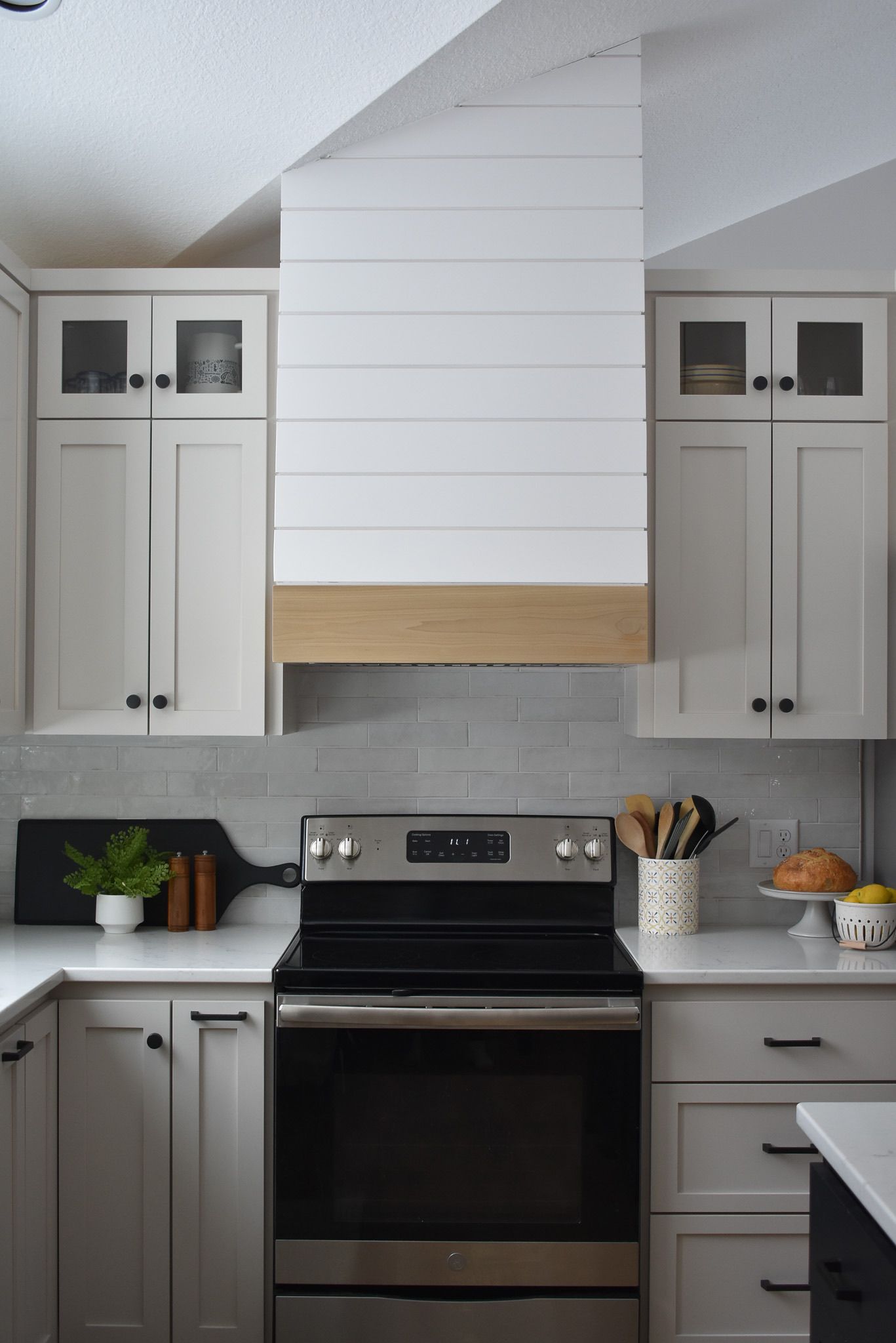 Kitchen with light gray cabinets, white range hood, and stainless steel oven.