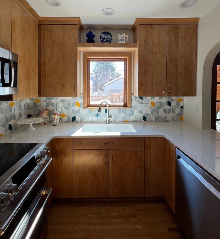 Kitchen with wooden cabinets, patterned backsplash, white countertops, and a window above the sink.