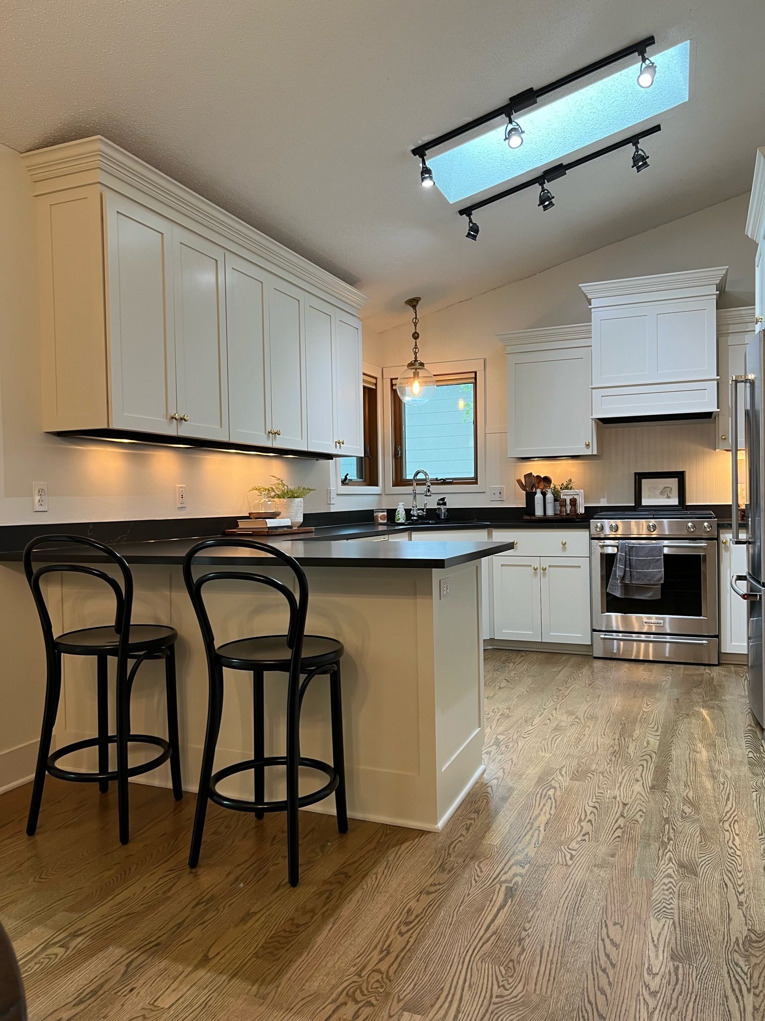 Kitchen with white cabinets, black countertops, wood floor, and two black bar stools.