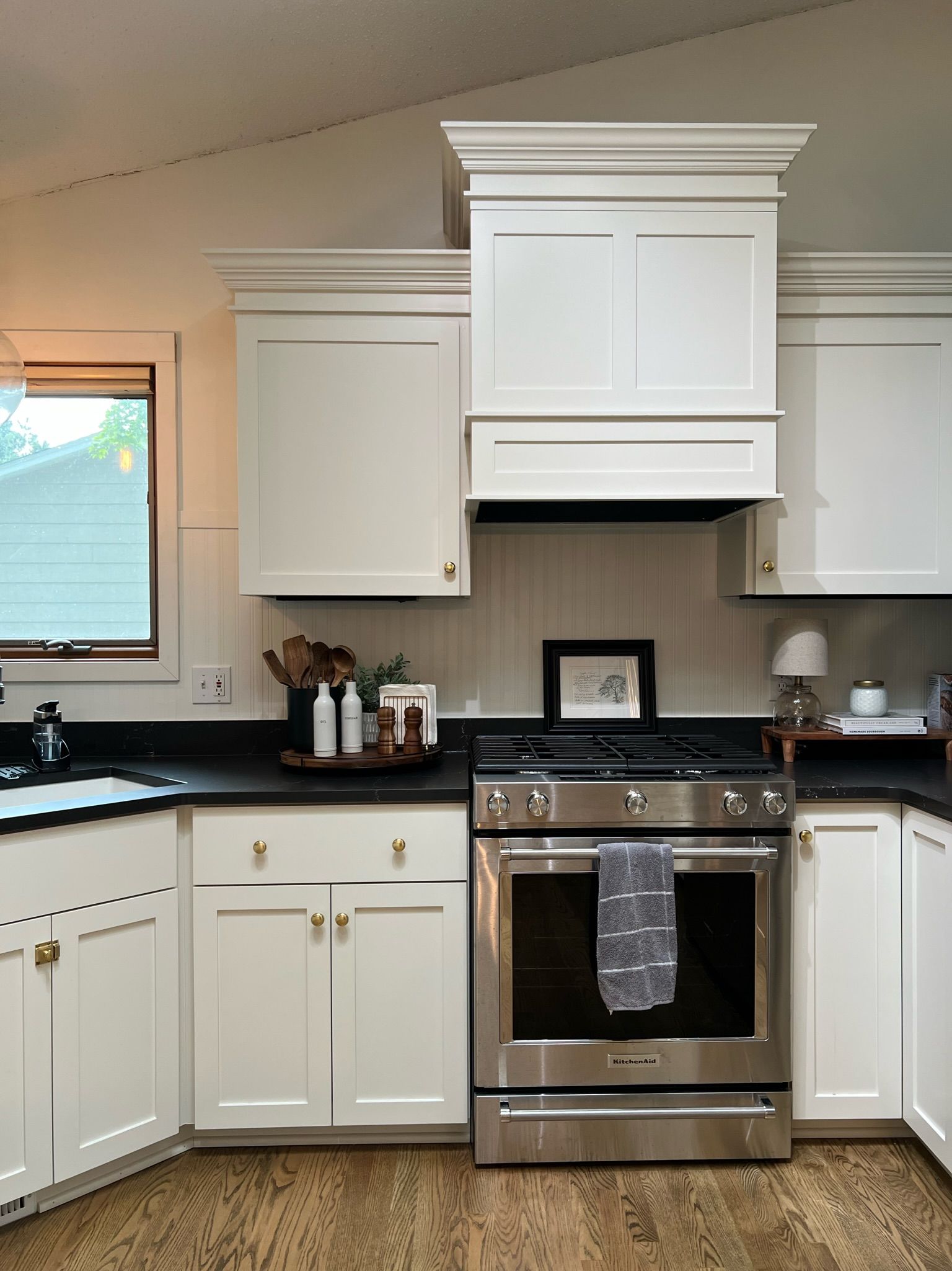 White kitchen with black countertops, stainless steel appliances, and wooden floors.