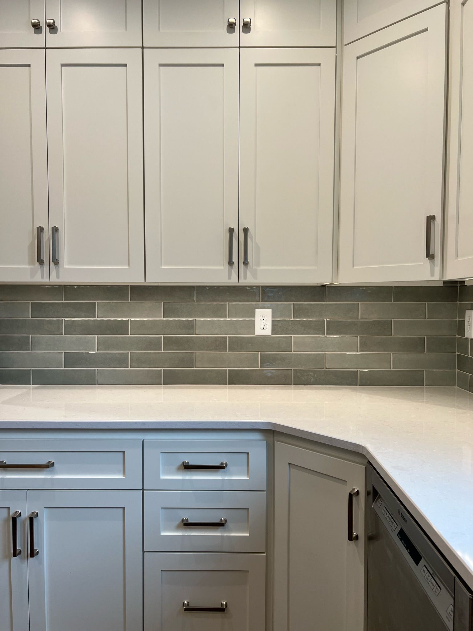 White kitchen cabinets with gray-green backsplash, and light countertop.