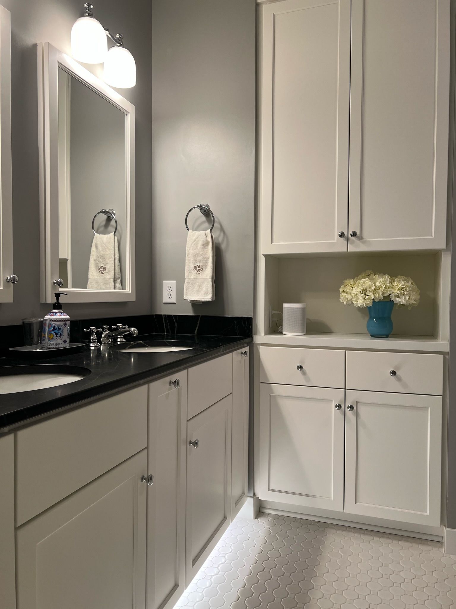 Bathroom with white cabinets, dark countertop, gray walls, and a large mirror.