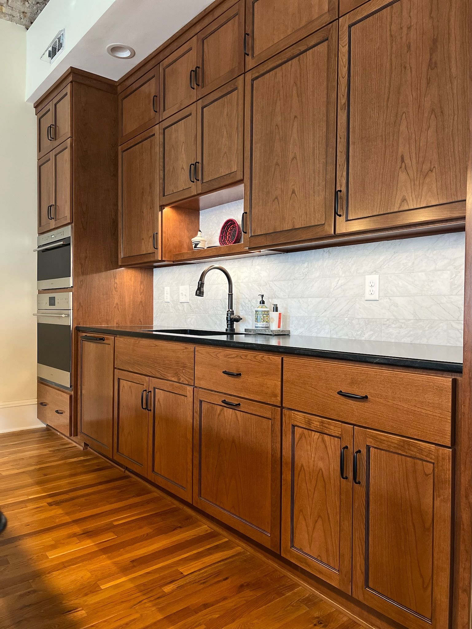 Wooden kitchen cabinets with black countertops and a black faucet.