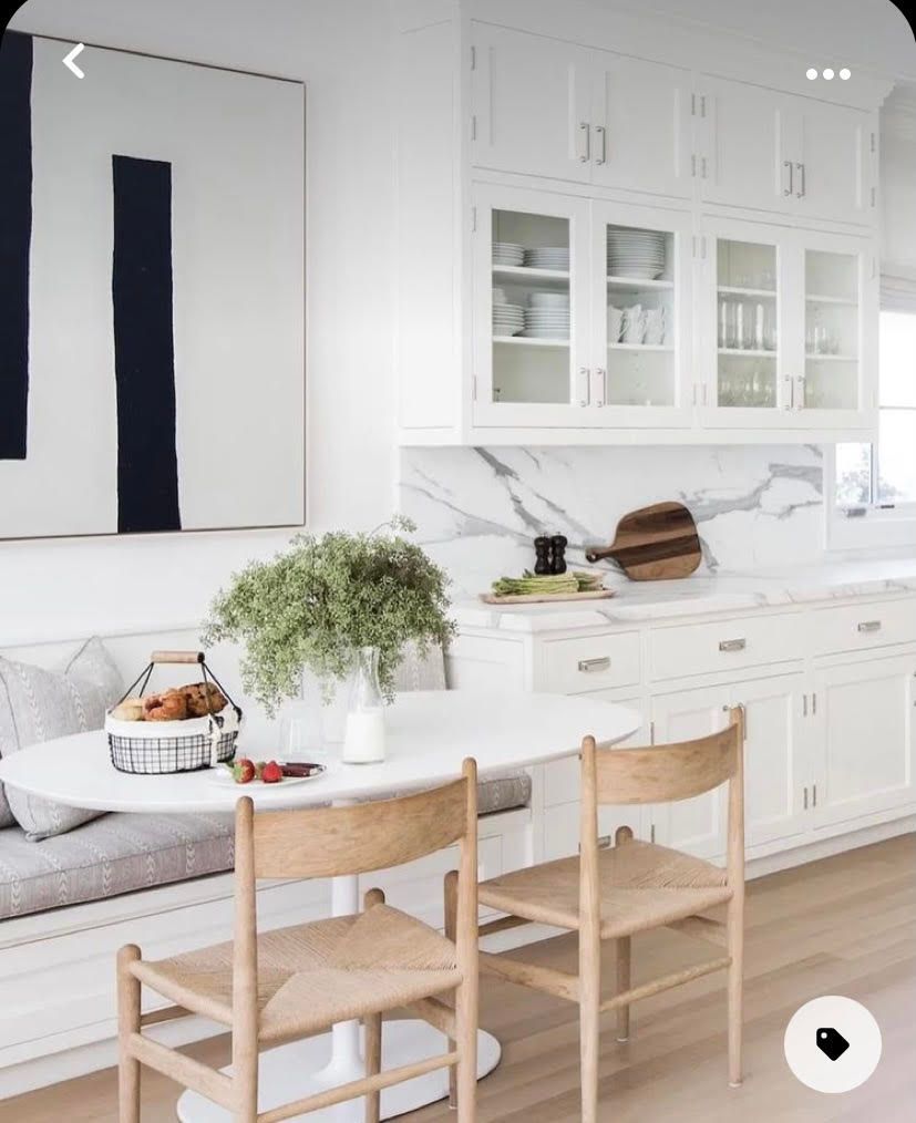 White kitchen with marble countertops, built-in cabinets, oval table, wooden chairs.