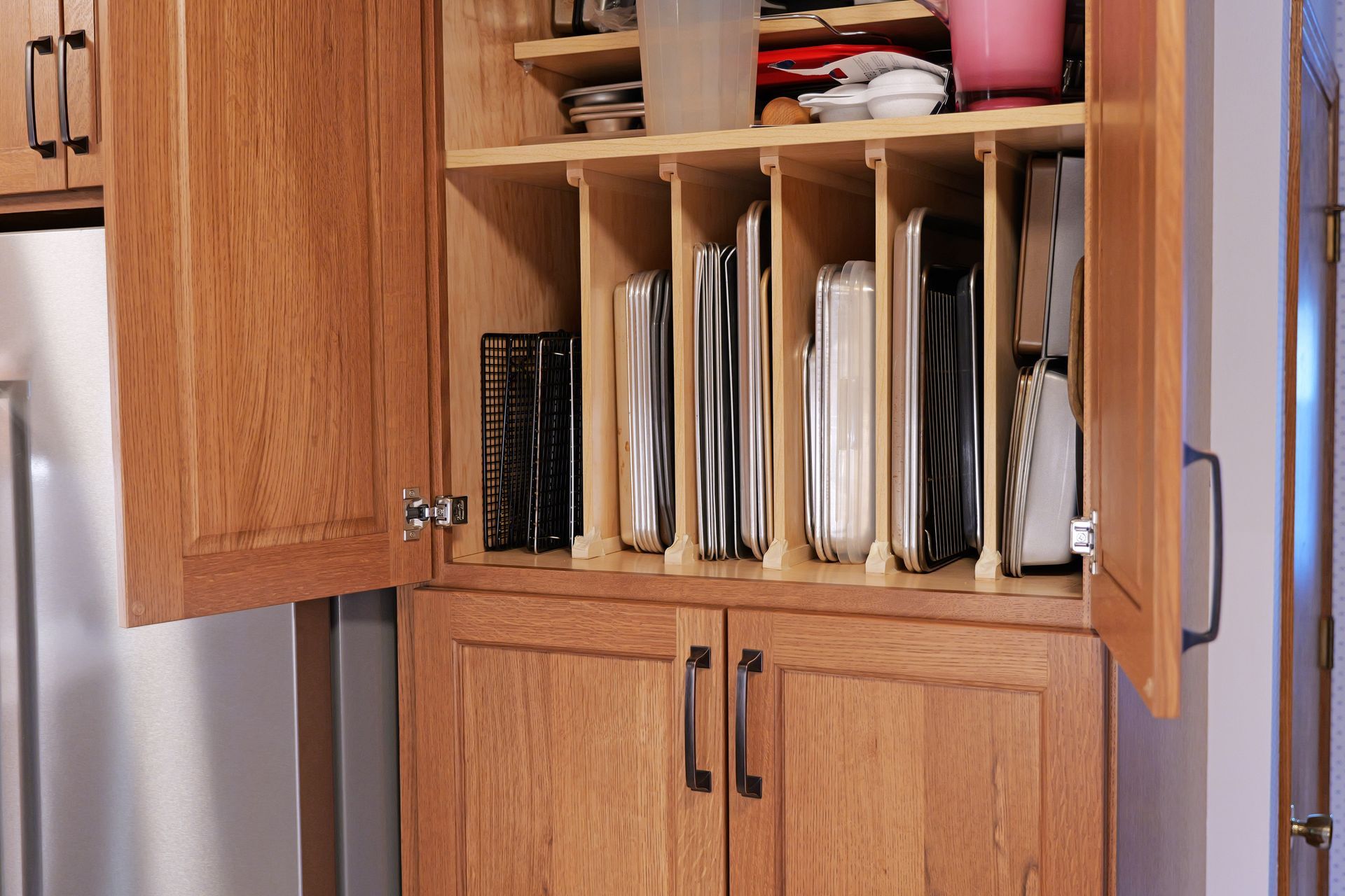 Oak kitchen cabinet with dividers for storing baking sheets and pans.