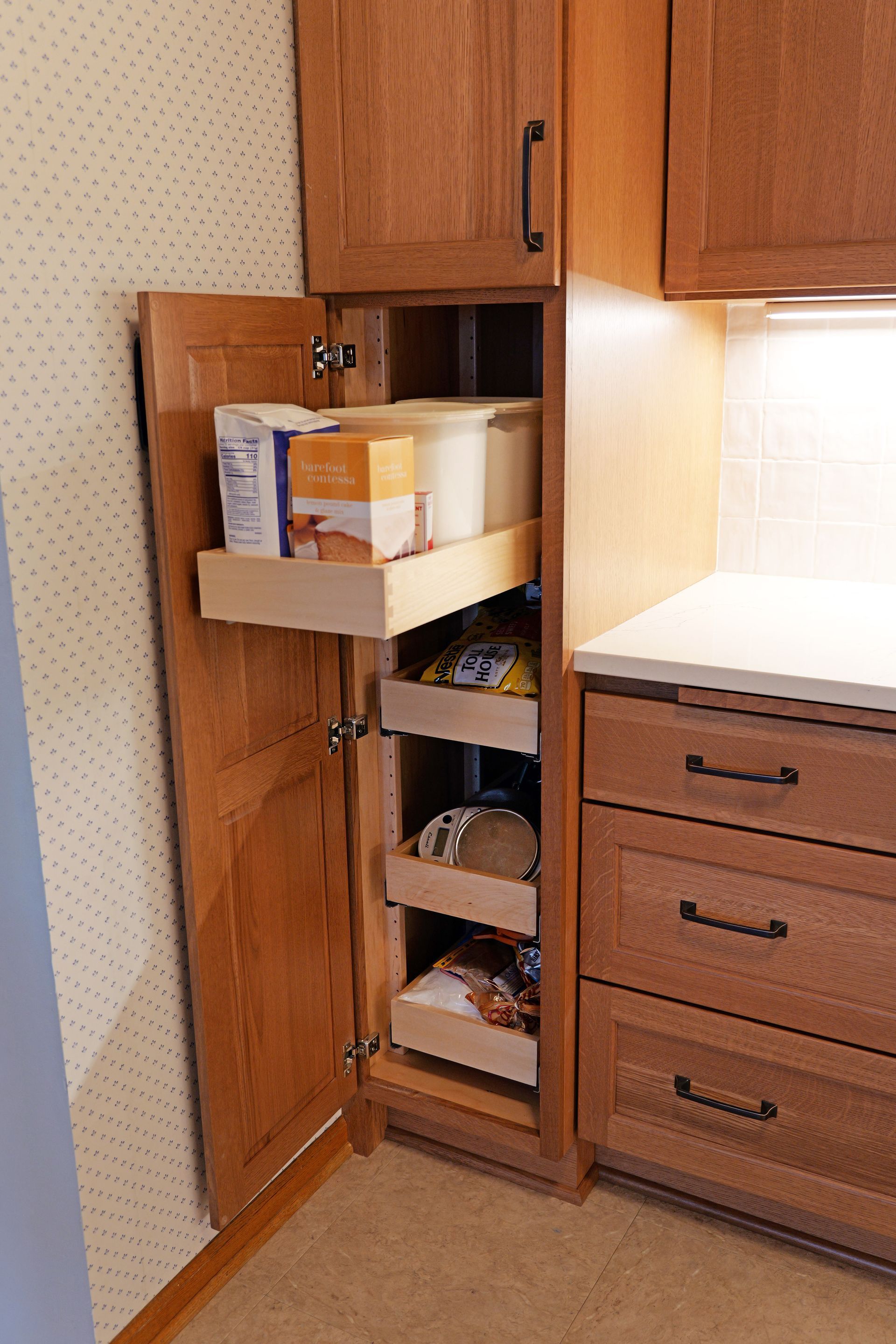 Kitchen pantry cabinet with pull-out shelves holding food items, next to drawers and countertop.