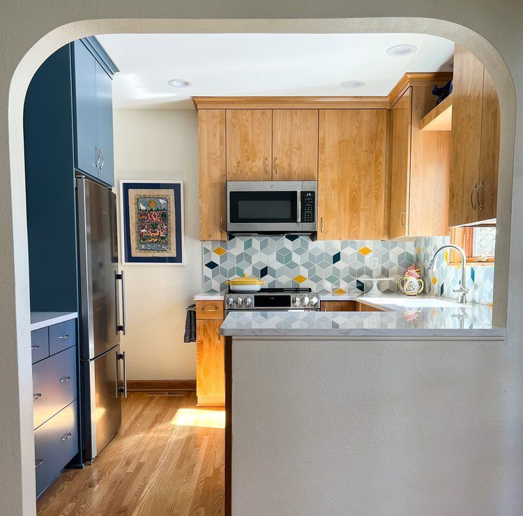 Kitchen interior with wood cabinets, blue tall cabinet, stainless steel appliances, and colorful tile backsplash.