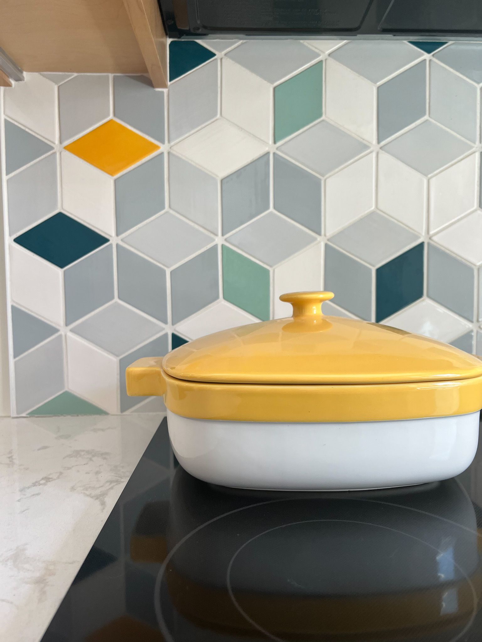 Yellow pot on stovetop in front of a geometric tile backsplash with teal, gray, and yellow accents.