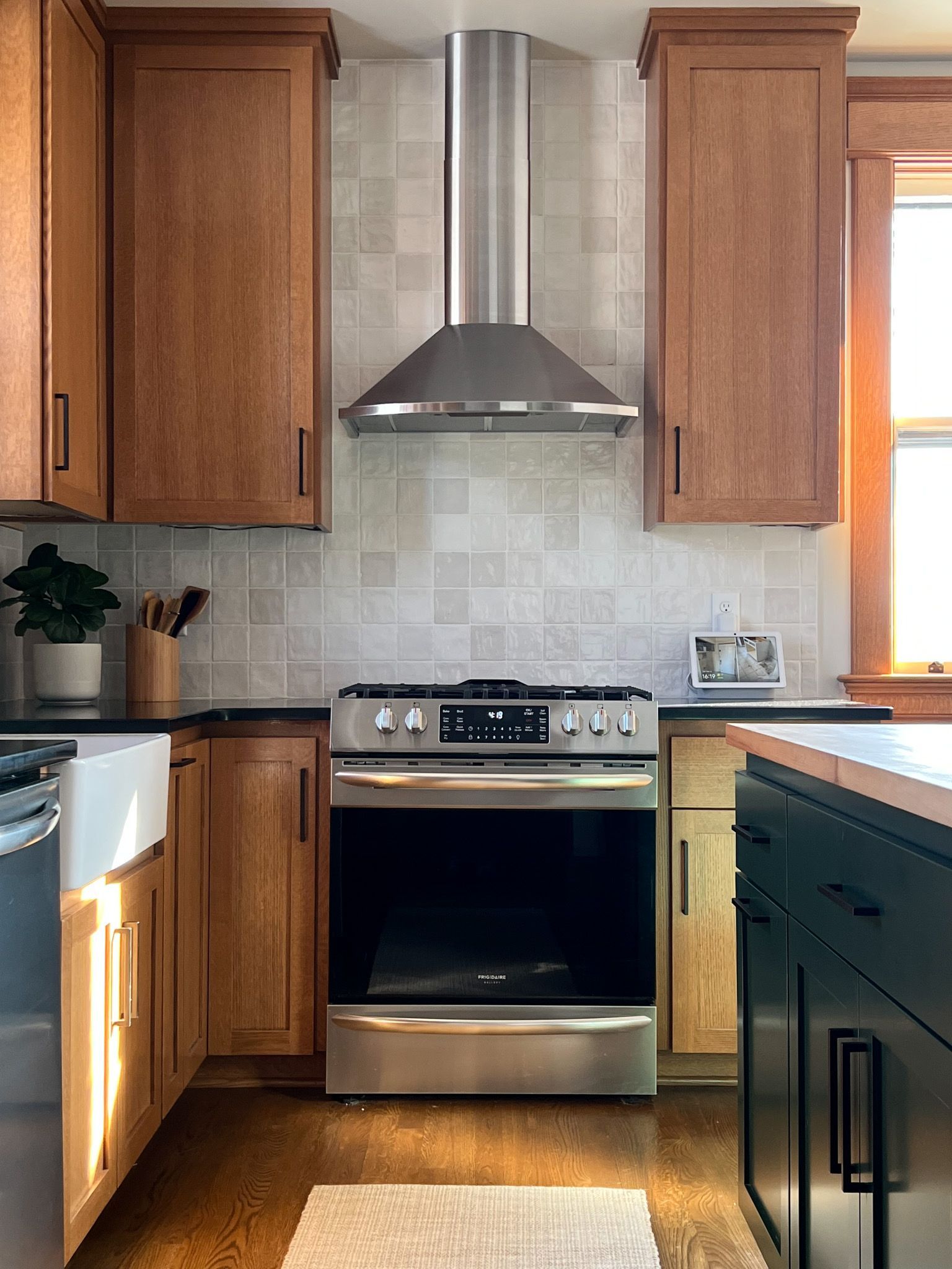 Kitchen with stainless steel range, hood, and light wood cabinets against a neutral tile backsplash.
