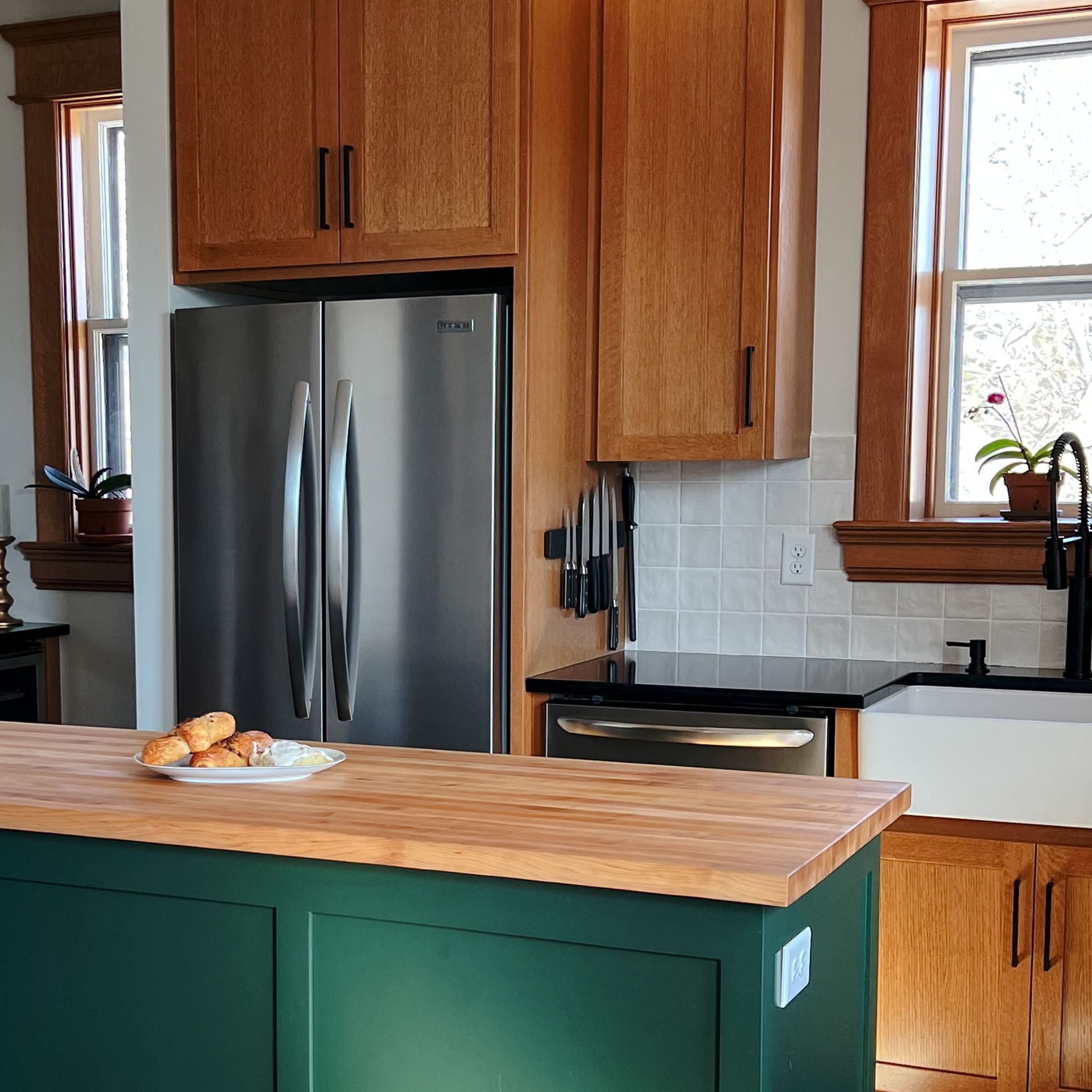 Kitchen with green island, stainless steel refrigerator, and wooden cabinets.