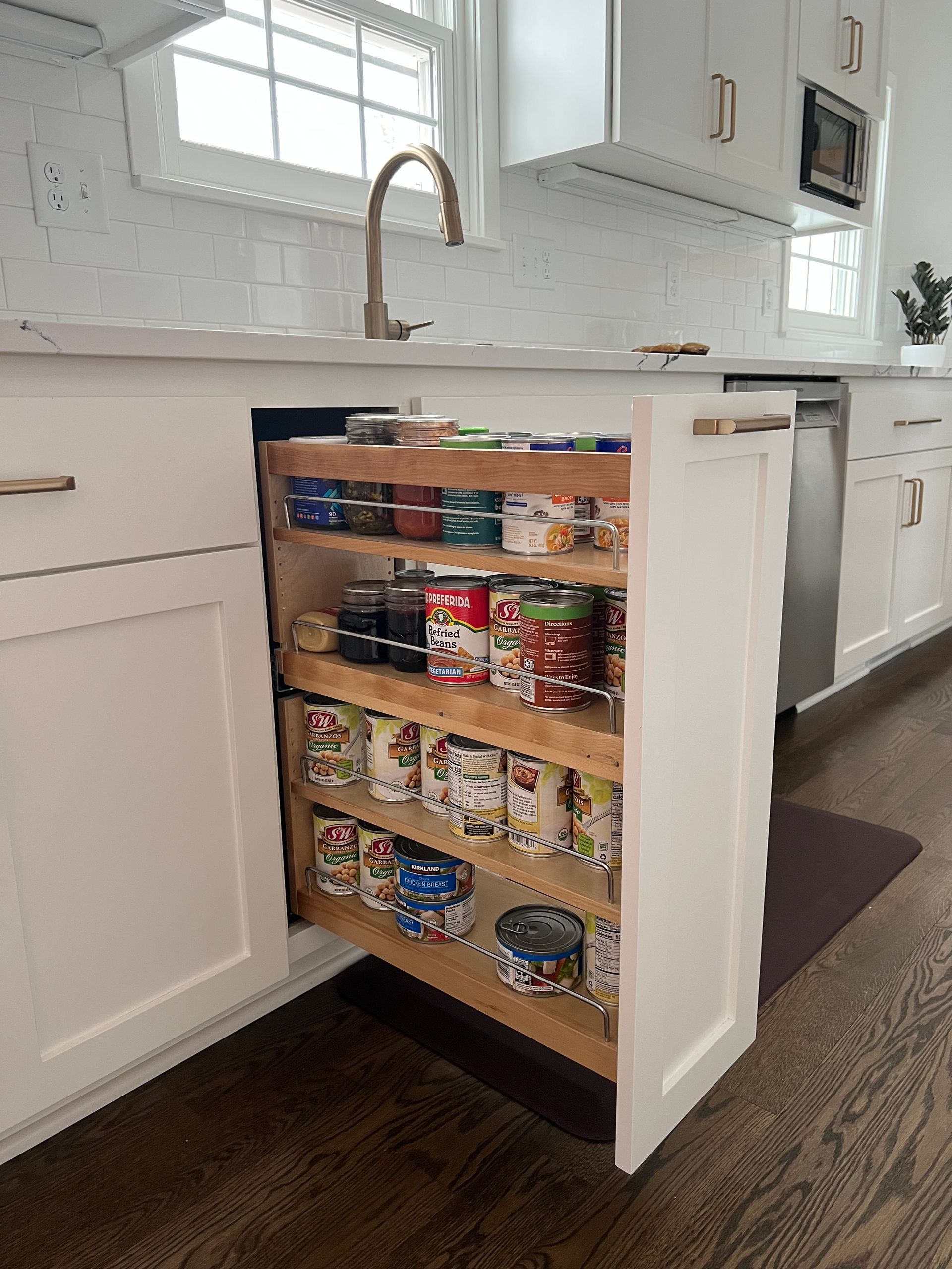White kitchen with a pull-out pantry holding canned goods, next to the sink and a dishwasher.