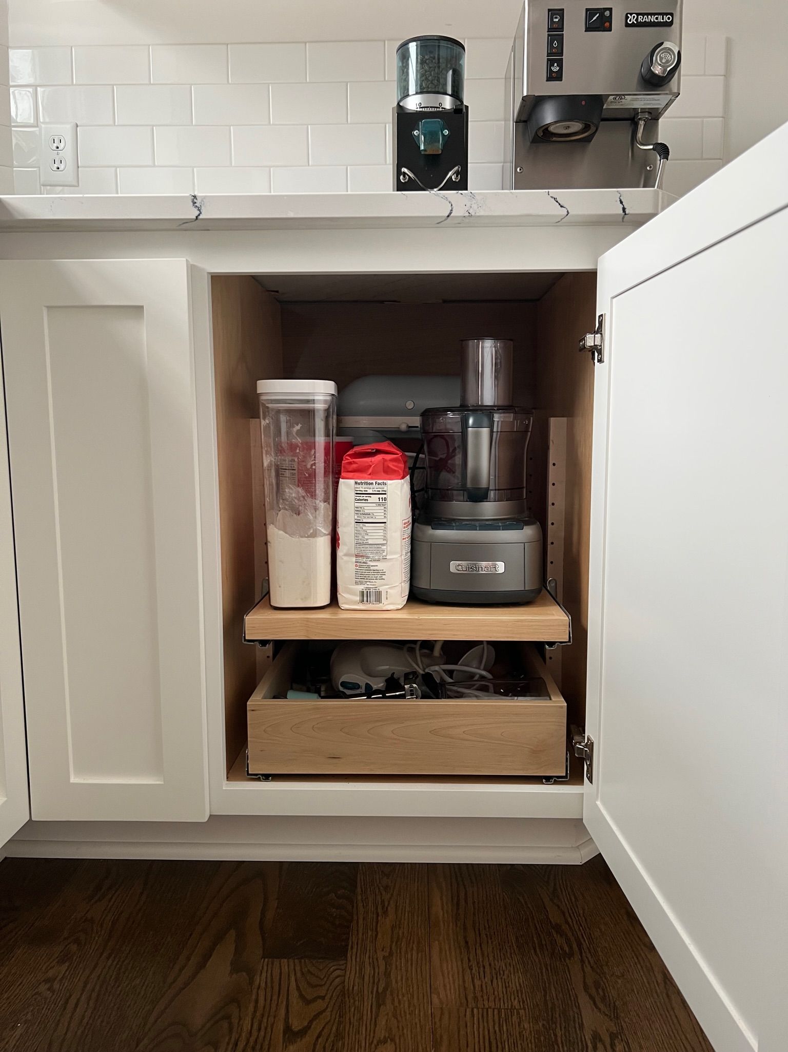 Kitchen cabinet with pull-out shelf holding food processor and canisters, with a drawer below for accessories.