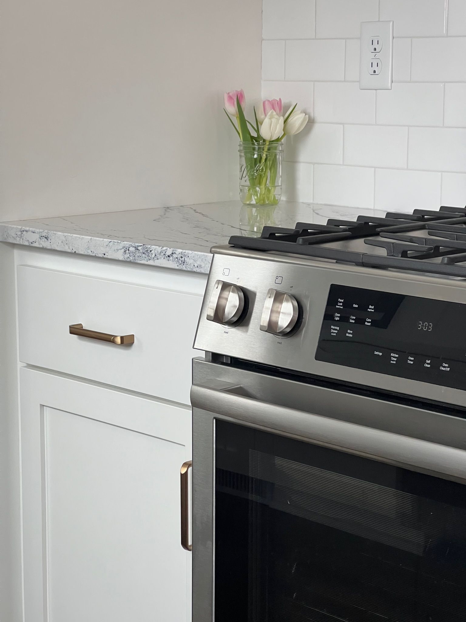 White kitchen with stainless steel oven, white cabinets, marble countertop, and flowers.