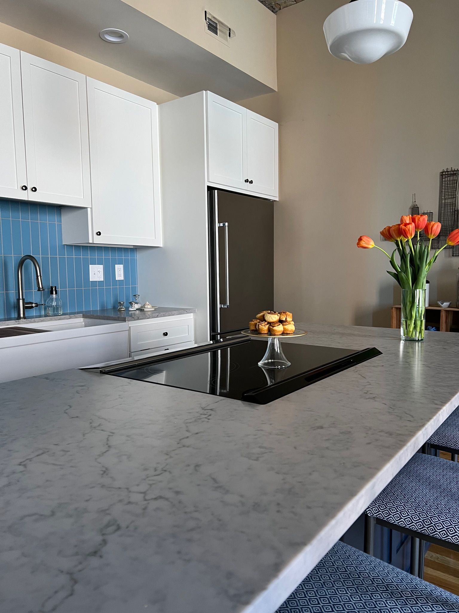 Modern kitchen with white cabinets, blue tile backsplash, gray countertop, and orange tulips.
