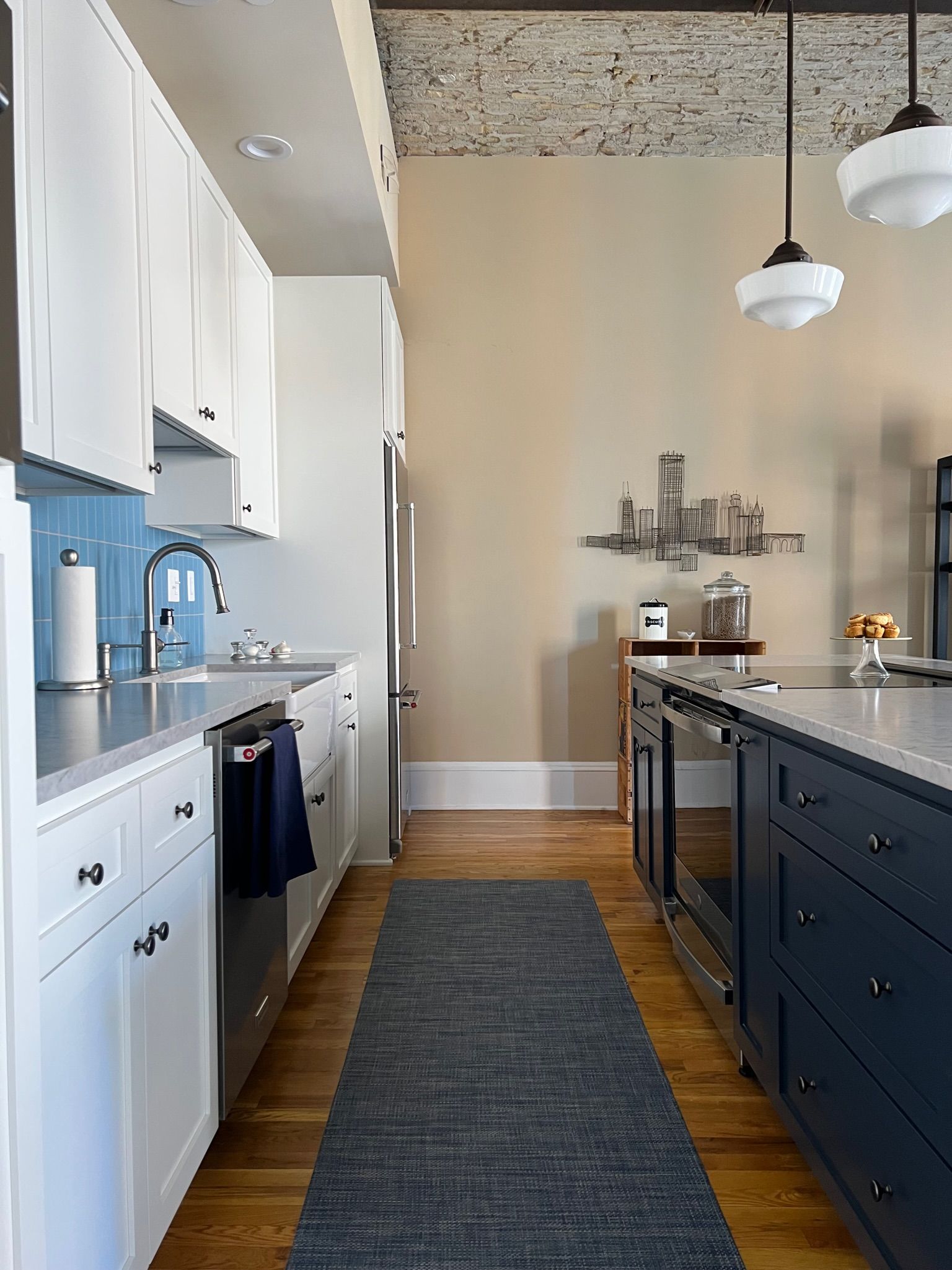 Modern kitchen with white and navy cabinets, stainless steel appliances, and wood floor.