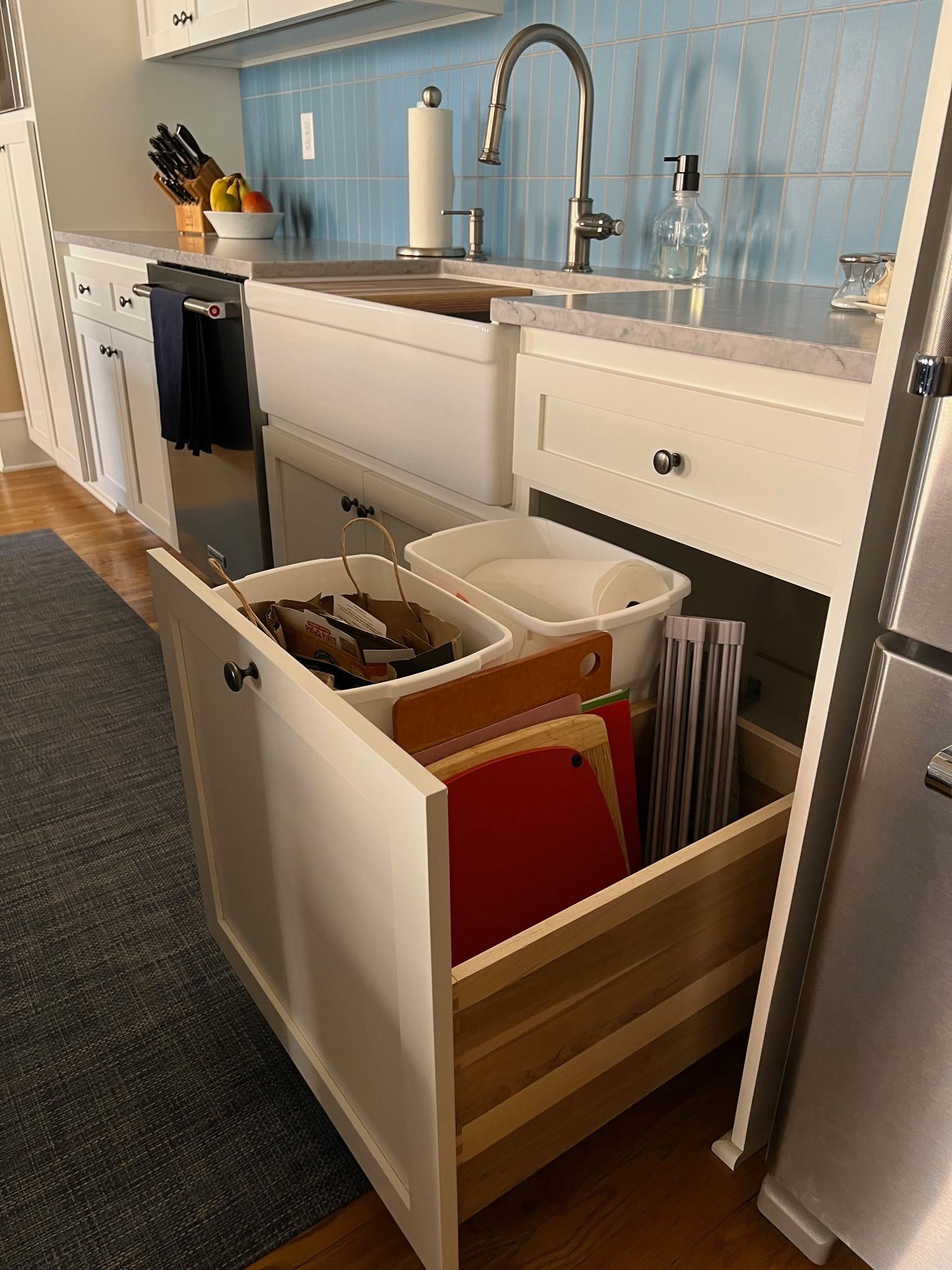 Pull-out kitchen cabinet with trash/recycling bins and cutting boards; light wood and white.