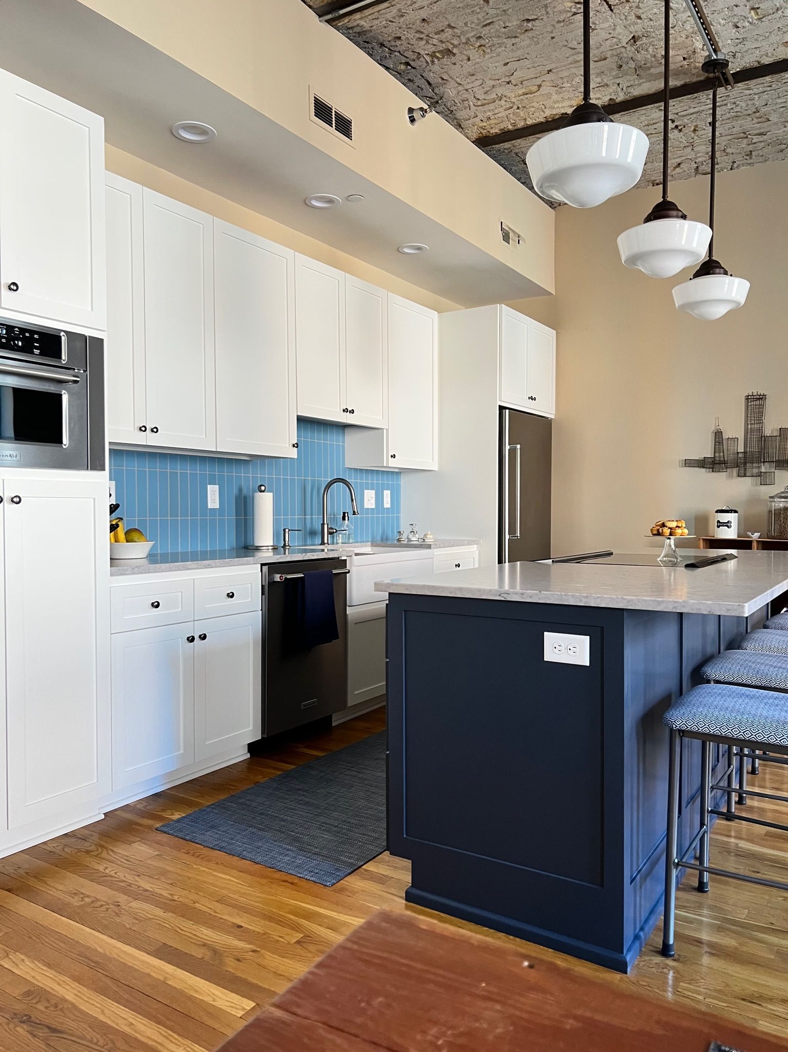 Modern kitchen with white cabinets, blue backsplash, navy island, and hardwood floors.