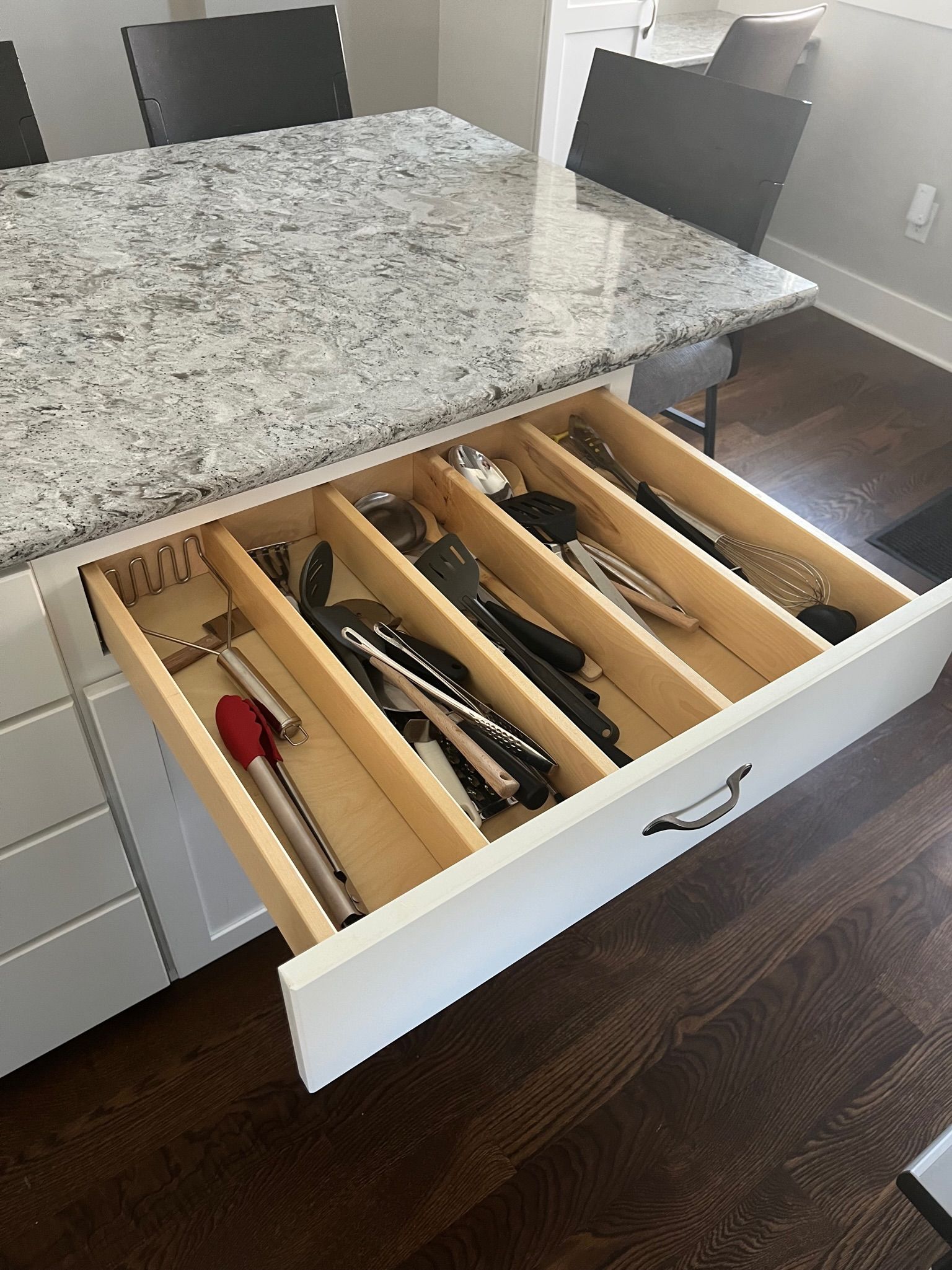 Open kitchen drawer with silverware, located beneath a granite countertop.