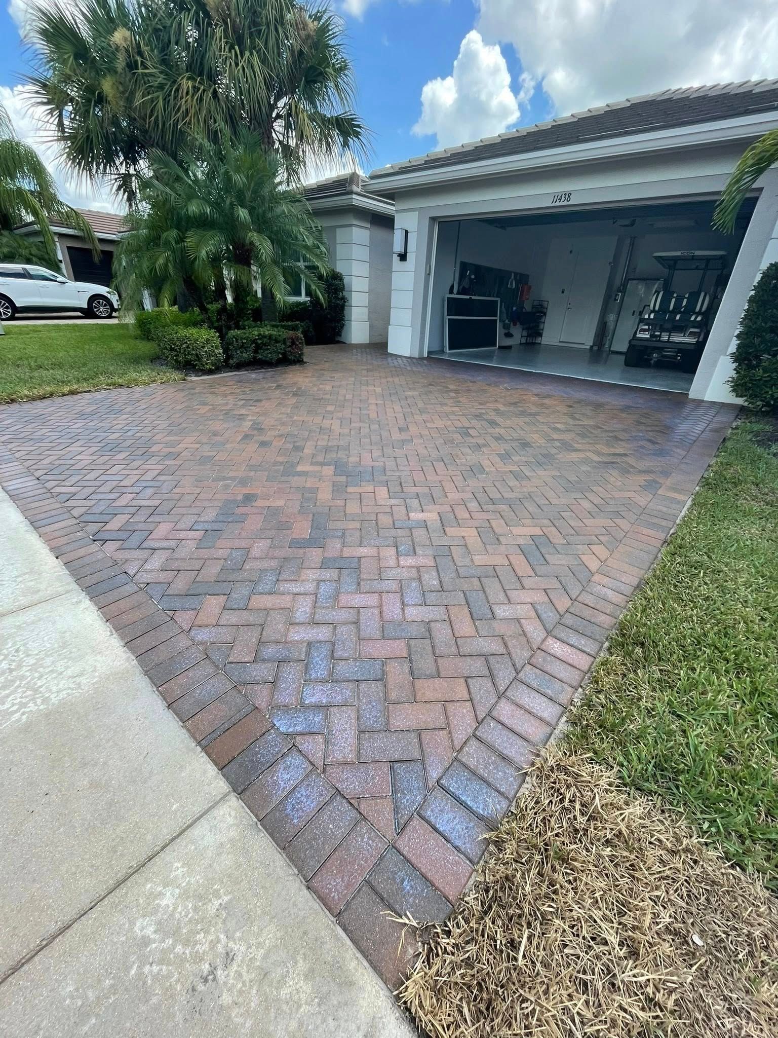 Brick driveway leading to a garage with open doors, in front of a house, on a sunny day.