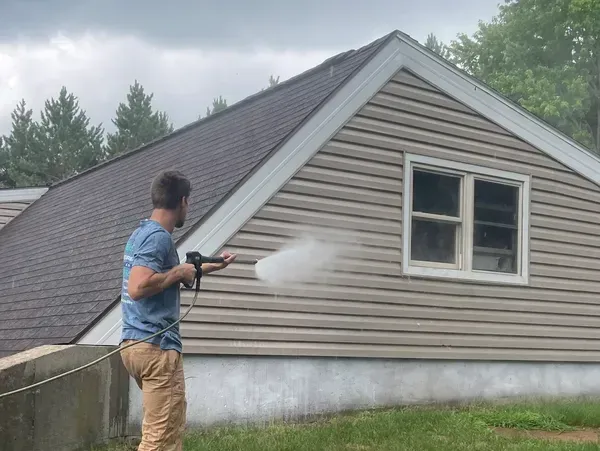 A man is cleaning the side of a house with a pressure washer. A man is cleaning the side of a house with a pressure washer.