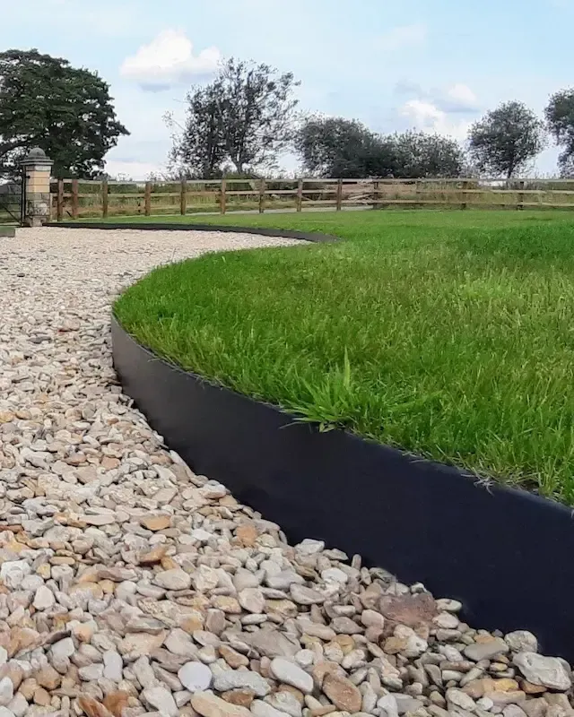 A black lawn edging is surrounded by gravel and grass