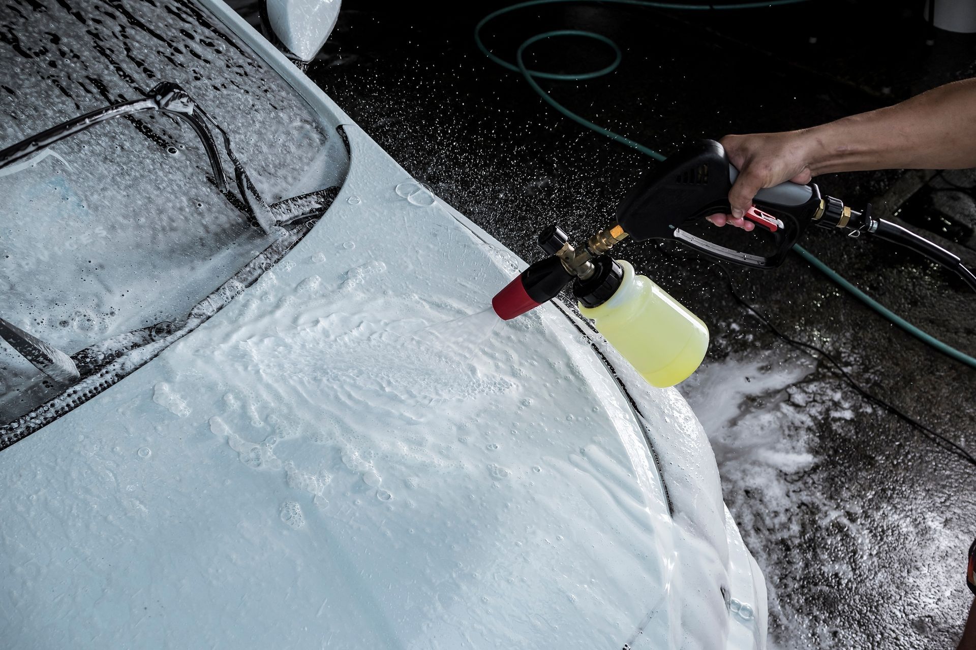 Person using a foam sprayer to wash a car covered in suds