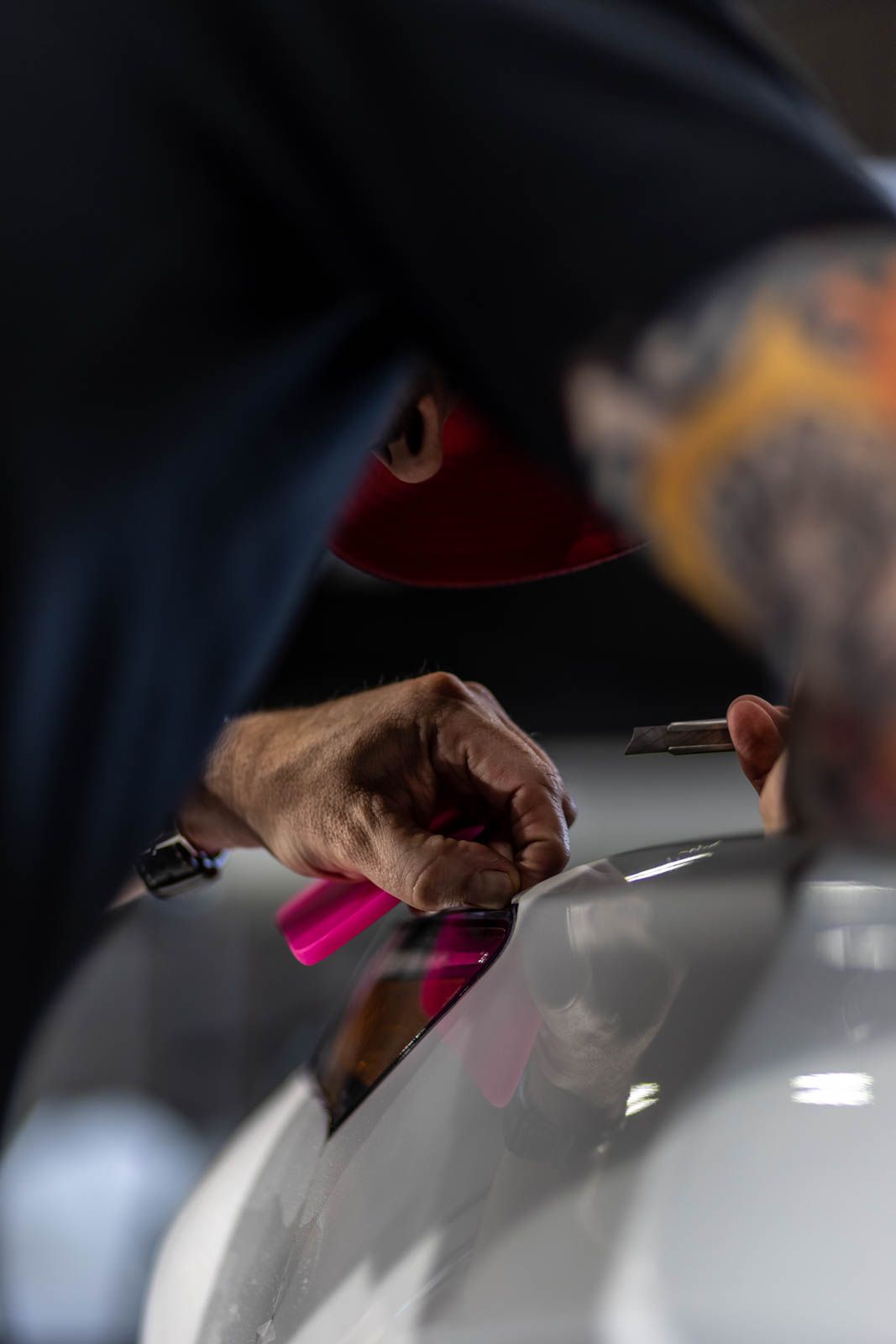 Hands working on a white car body with a pink tool in an auto repair shop