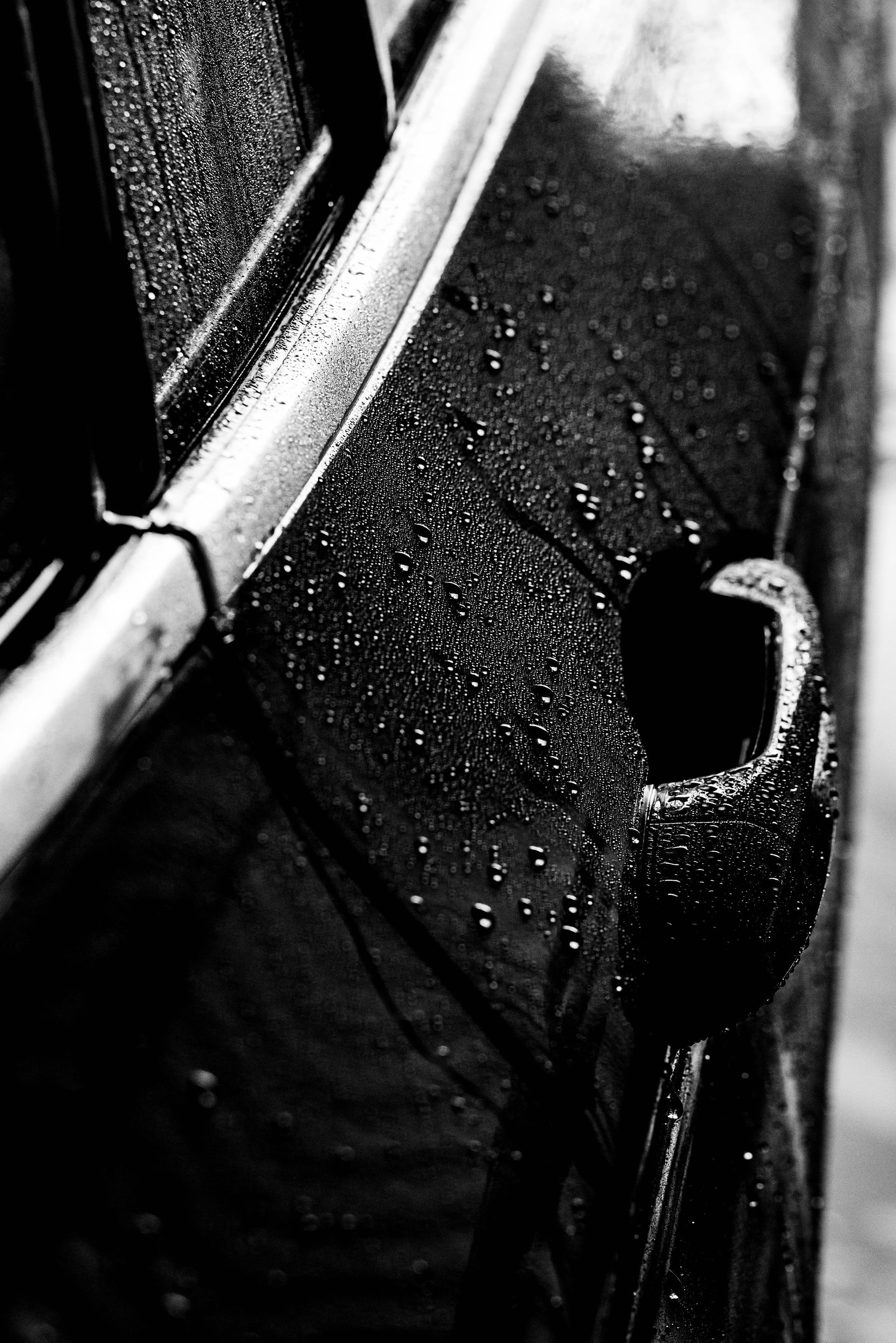 Close-up of a black, wet car body panel with raindrops and a curved chrome trim.