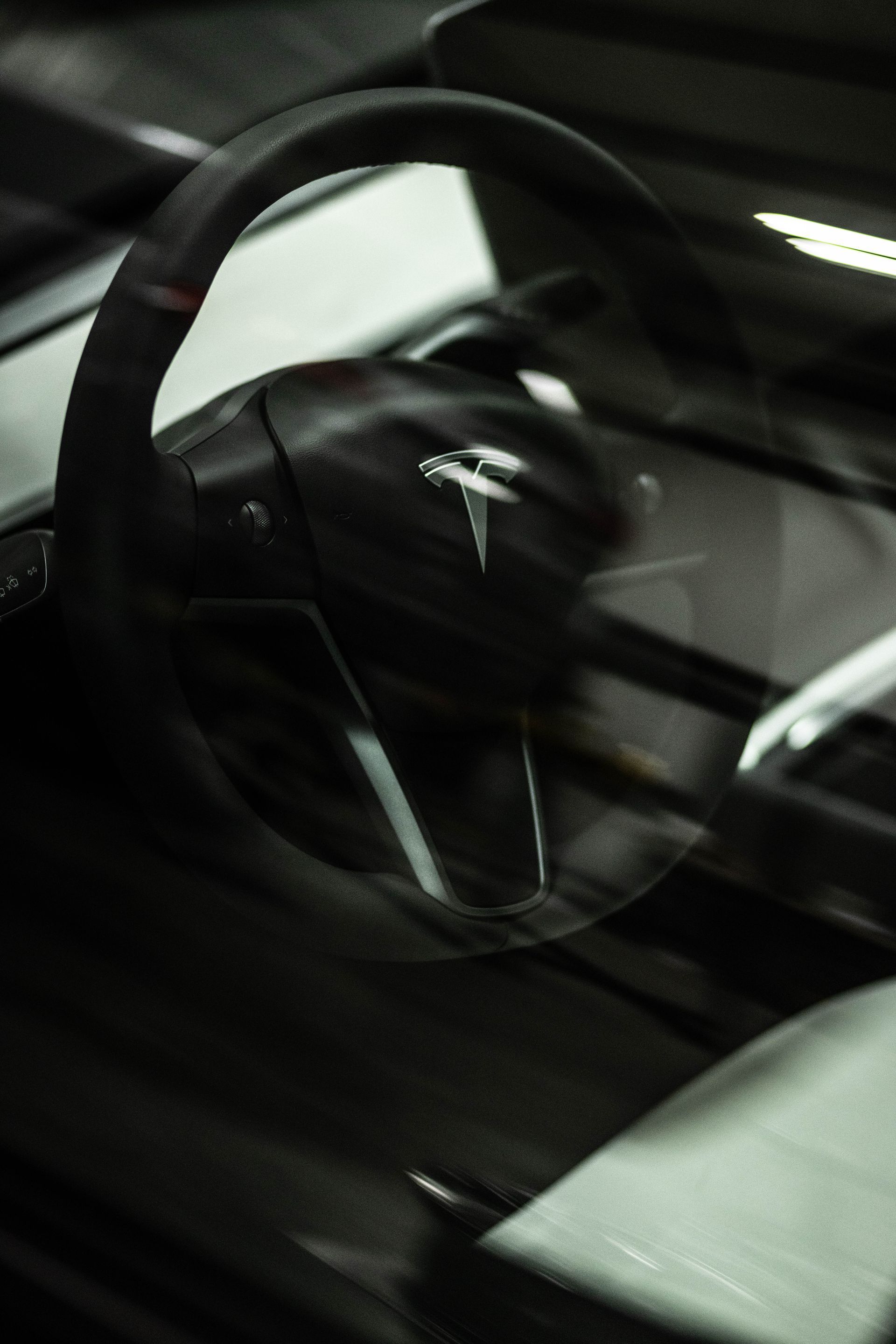 Black Tesla steering wheel and dashboard viewed through a car window at night