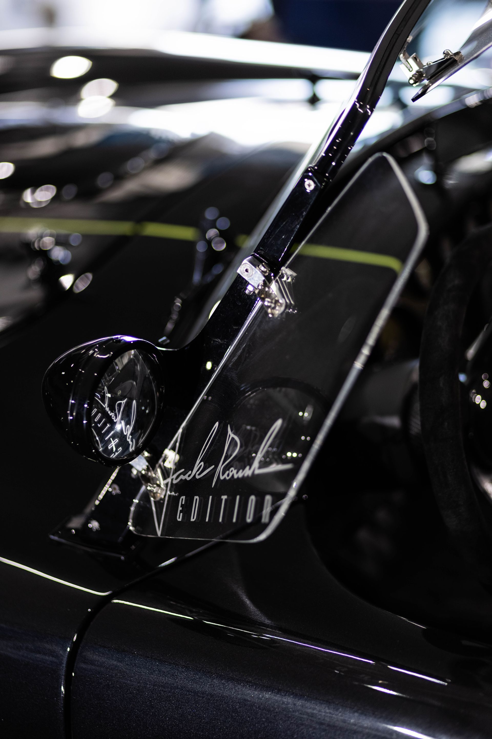 Close-up of a glossy black car door and side mirror with a gold signature decal.