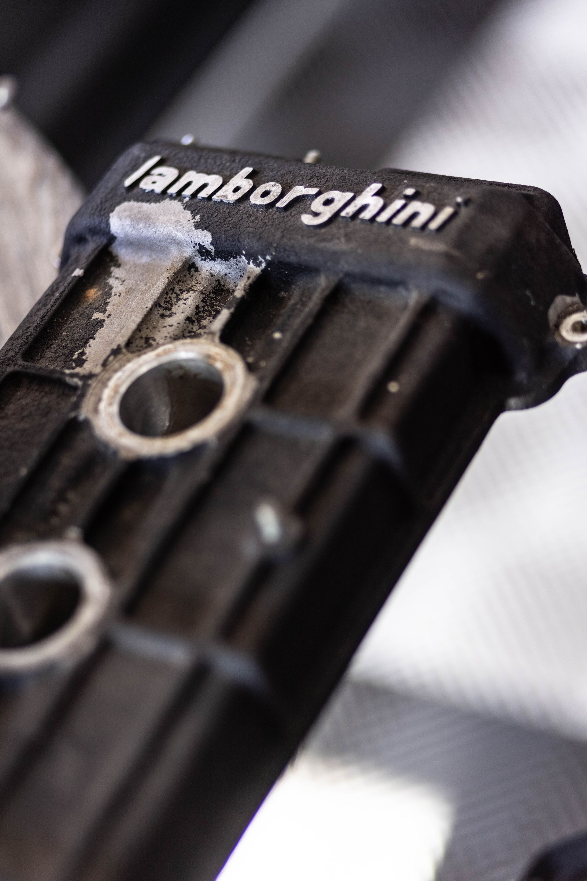 Close-up of a black Lamborghini-branded key fob with a silver ring on a textured surface