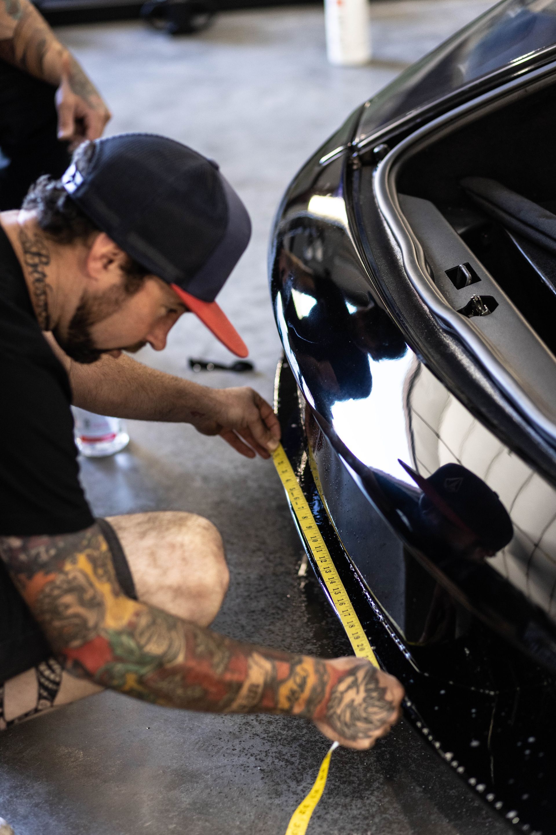 Person measuring a black car with a yellow tape measure in a garage
