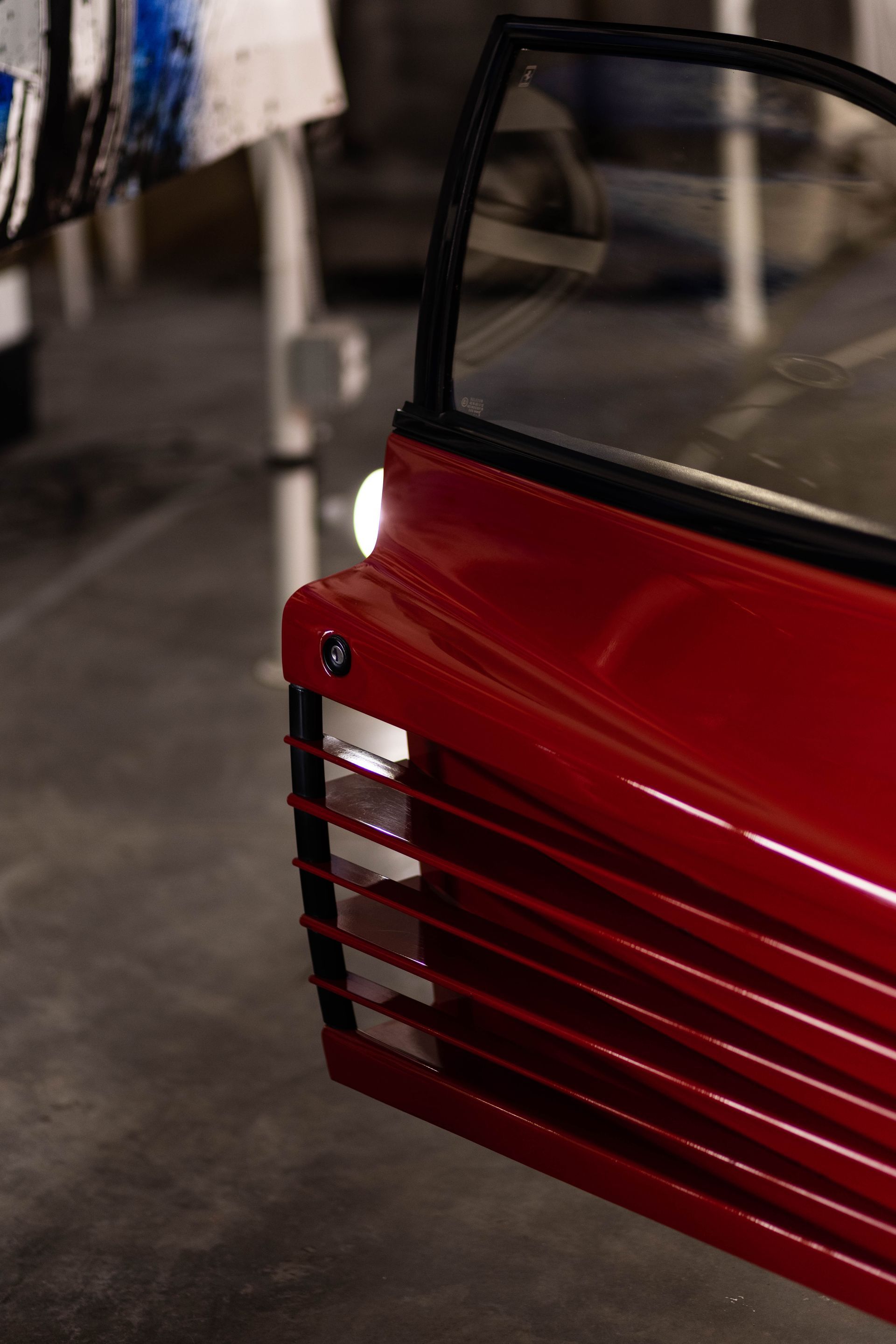 Red vented panel on a vehicle or machine, with a black handle against a blurred workshop floor.